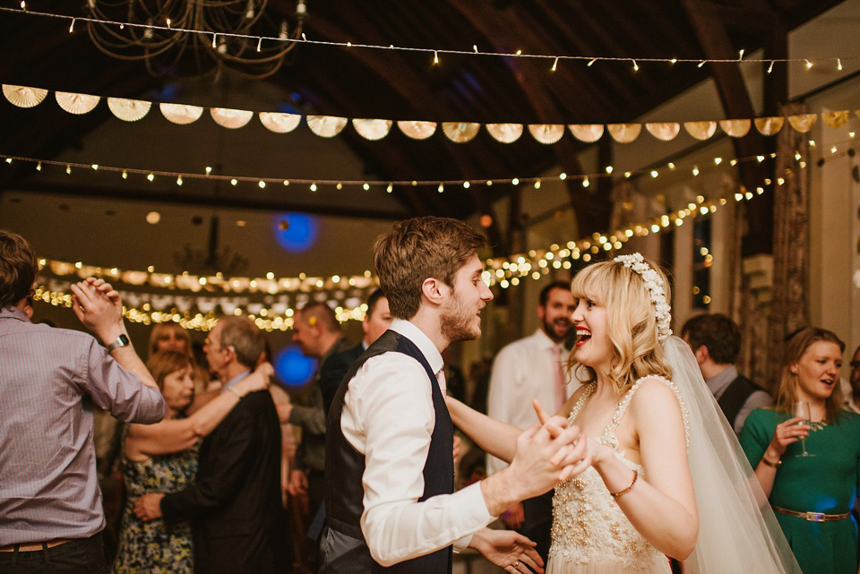 The bride wears a customised Alice & Olivia dress and 1950s wax flower headpiece for her Springtime village hall wedding. Photography by Ellie Gillard.