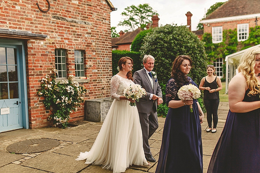 The bride wore a Watters wedding dress for her wedding at The Great Barn at Micklefield Hall in Hertfordshire. The bridesmaids wore navy blue. Photography by Benjamin Stuart.