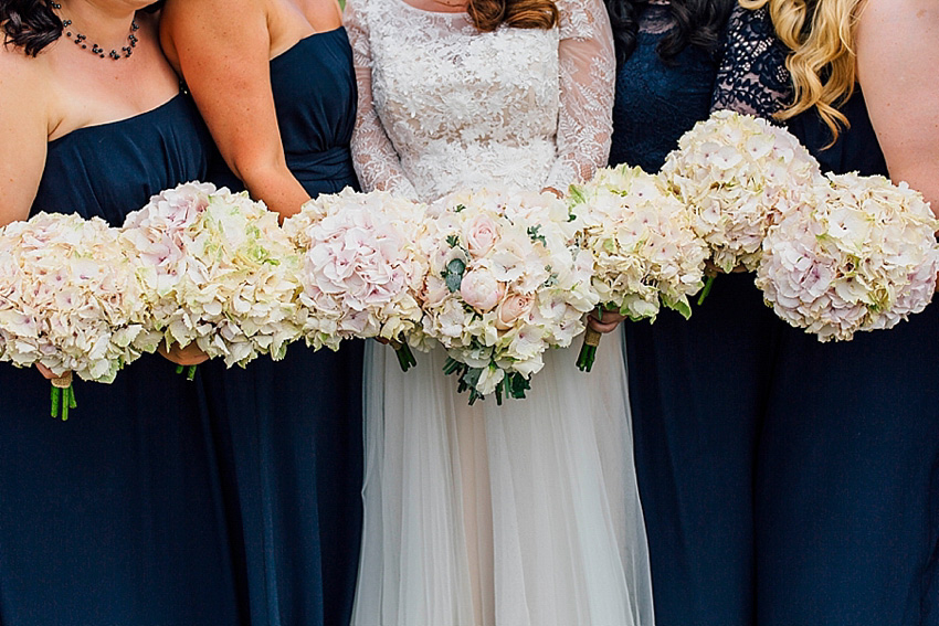 The bride wore a Watters wedding dress for her wedding at The Great Barn at Micklefield Hall in Hertfordshire. The bridesmaids wore navy blue. Photography by Benjamin Stuart.