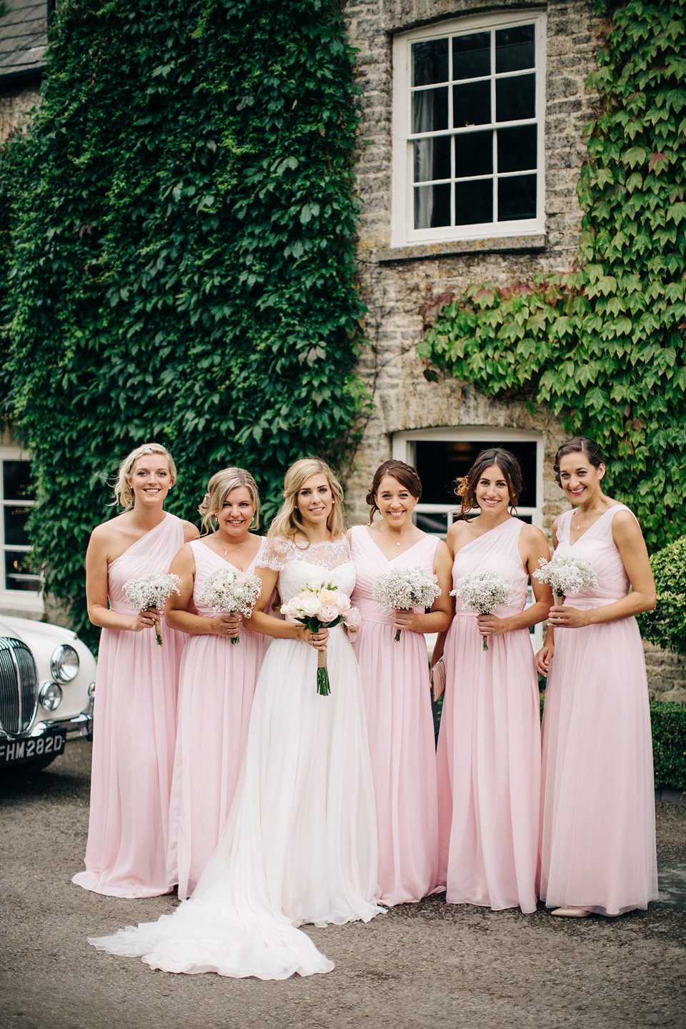 Bride Melanie wears the 'fleur' gown by Naomi Neoh for her Cripps Barn wedding. Her bridesmaids are most pretty in soft pink by 'For Her & For Him'. Images by M&J Photography.