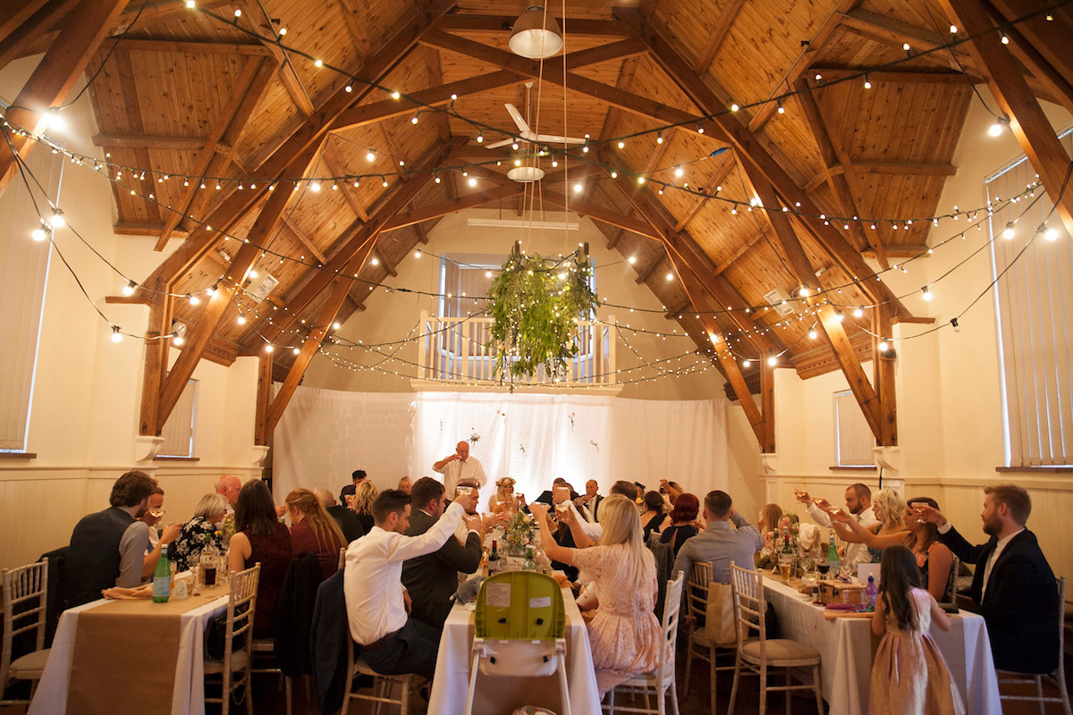 Bride Laura wore a Charlie Brear gown and floral crown for her charming Autumn village hall wedding. Photography by Henry Britten.