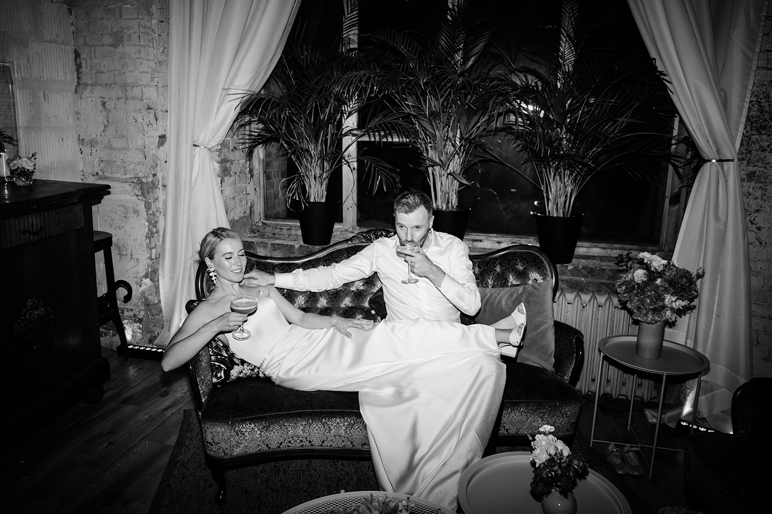 bride and groom sitting on a sofa drinking champagne
