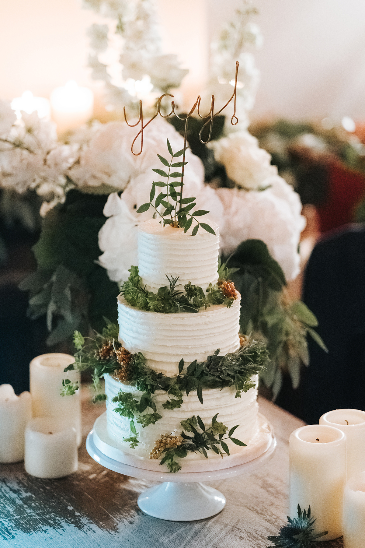 A 3 tier weding cake decorated with green leaves and a YAY cake topper