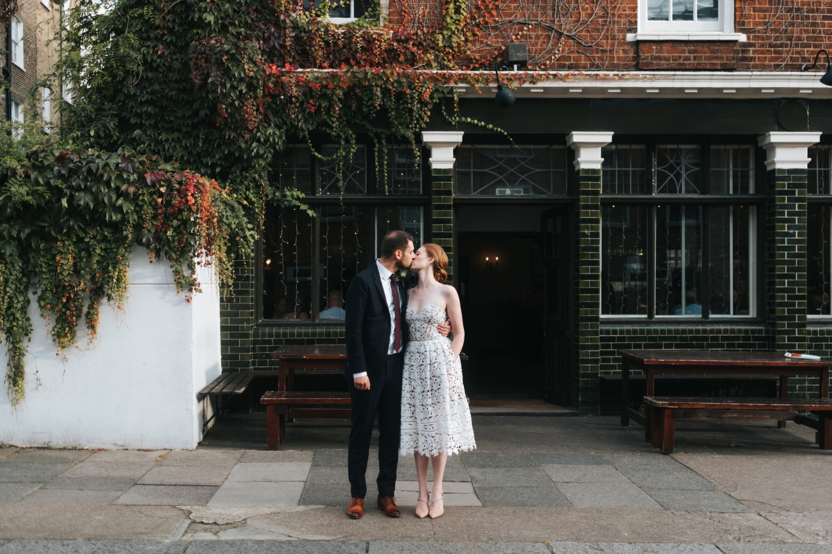 Modern bride and groom kiss outside a London pub