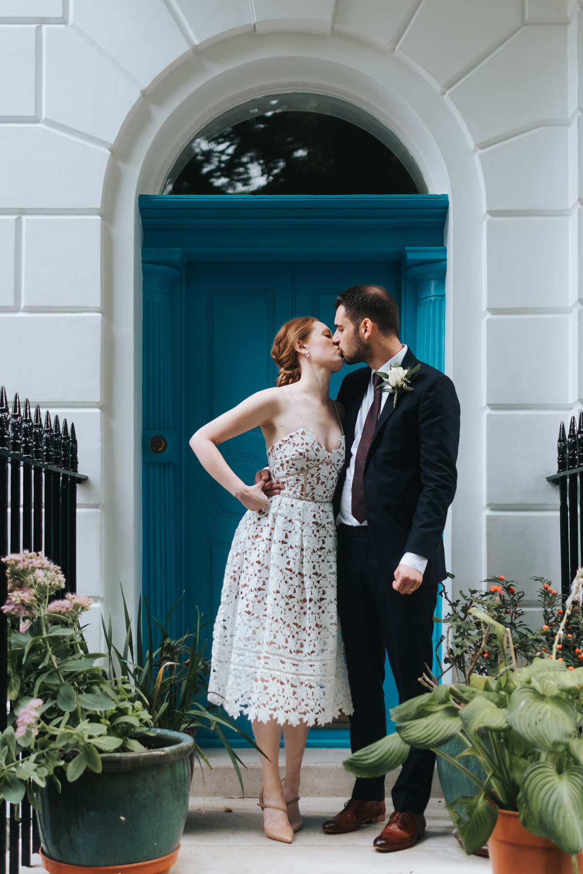 Modern bride and groom kissing outside a blue front door in London