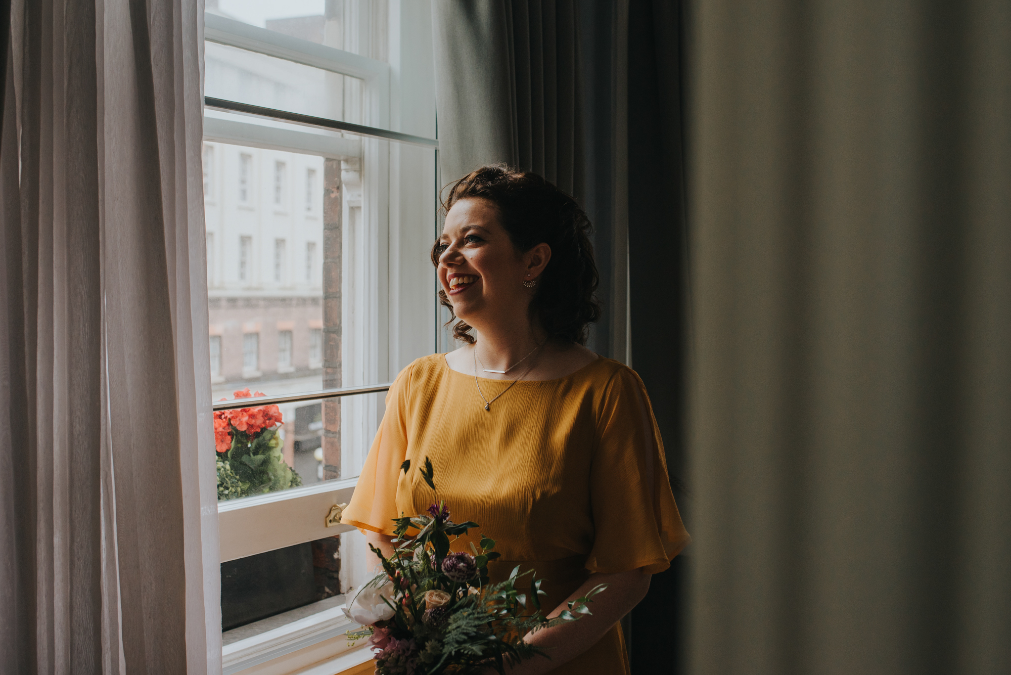 Bride in a yellow wedding dress looking out of a window