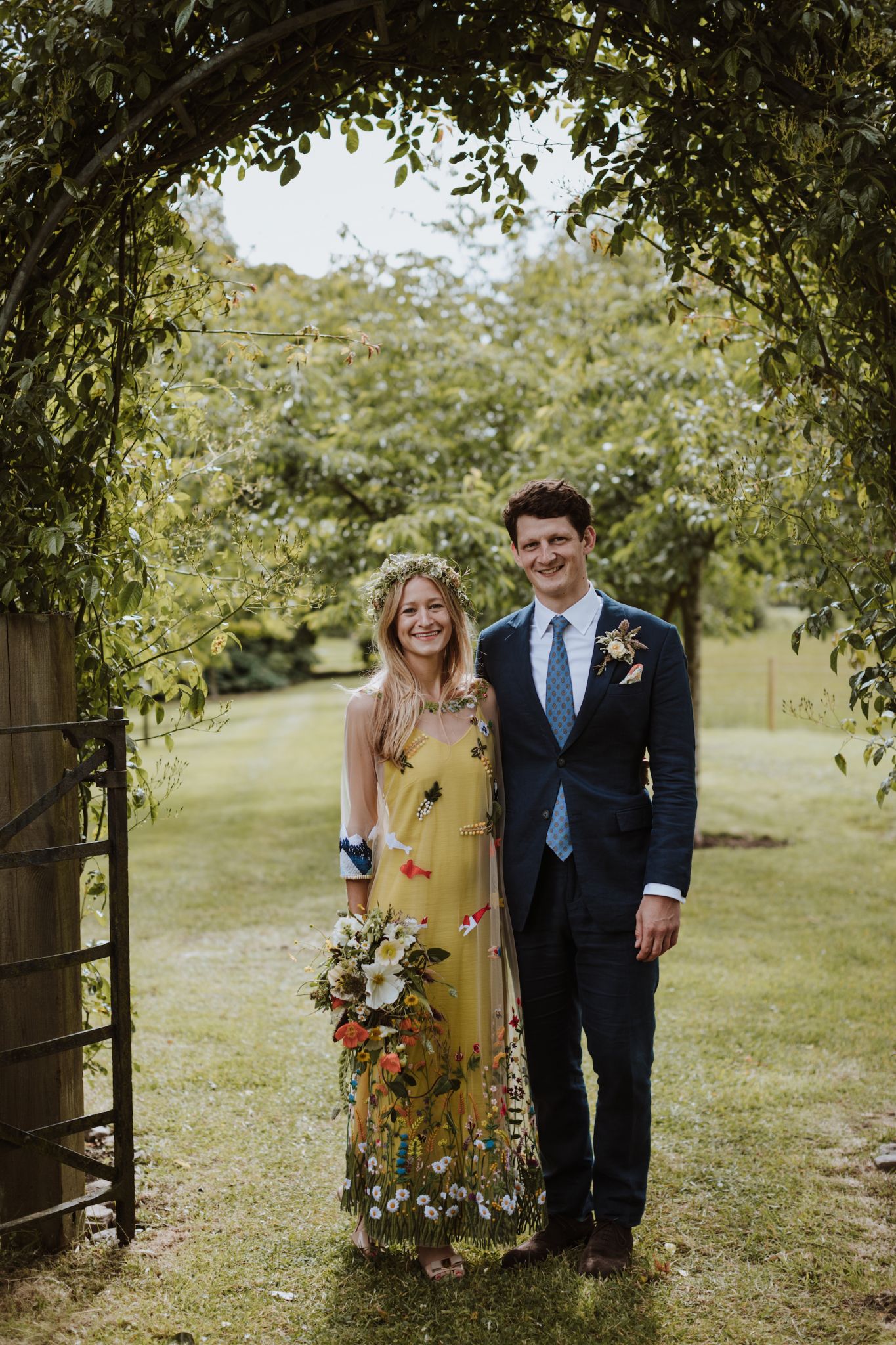 02 Yellow floral wedding dress bride groom standing under green leafy arch