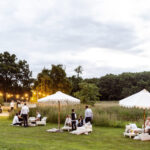 relaxed high end Outdoor wedding reception with festoon lighting around firepit and white parasols in the meadow at cotswolds wedding venue