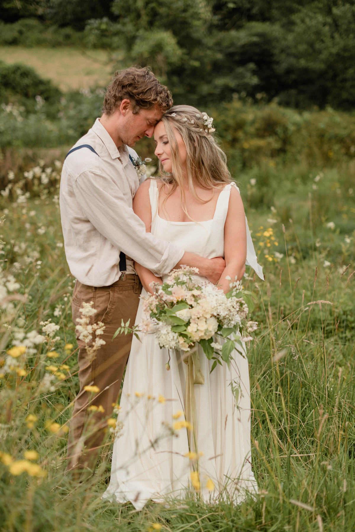 Camel Studio: County wedding venue in Cornwall. Bride & groom embracing. Bride has flower sin her hair & carries a natural wedding bouquet with silk ribbons. 