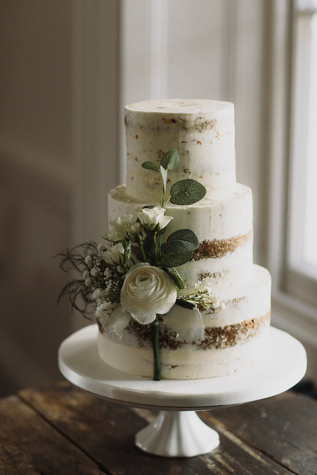3 tier naked wedding cake with white flowers and greenery