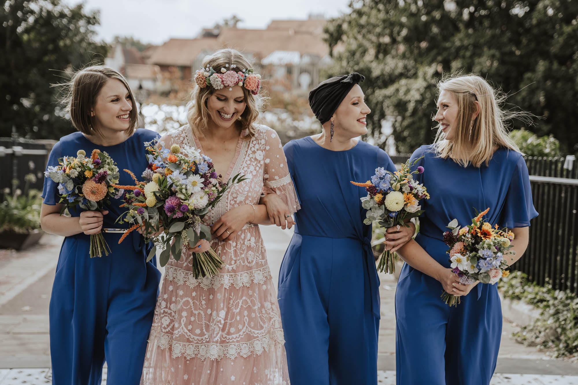 Bridesmaids in blue jumpsuits. Bride in pink Needle & Thread wedding dress.