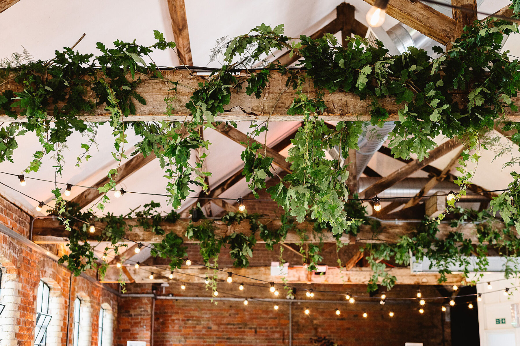 Foliage hanging from wooden beams inside Loft Warehouse wedding venue, London