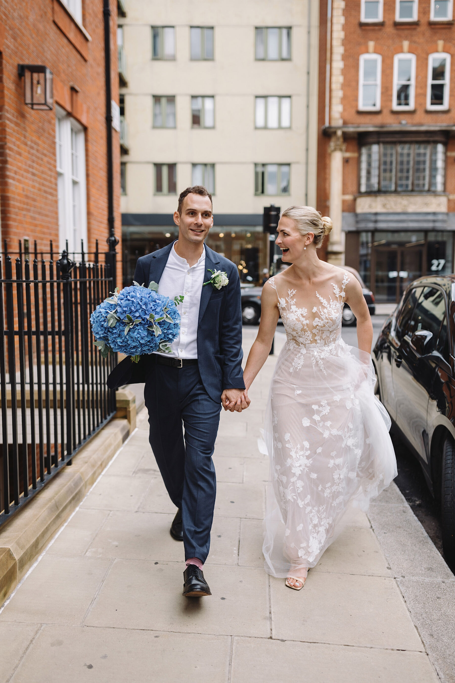 Groom in informal blue suit carrying bouquet of large blue hydrangea. Bride wears Anna Kara wedding dress. Wolf & Co. Photography.