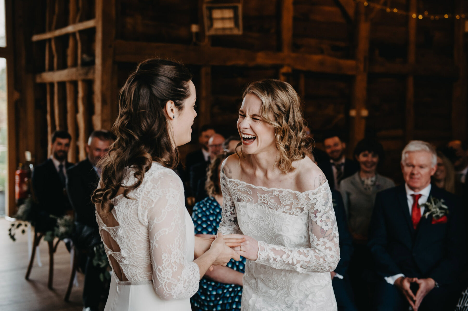 Two brides holding hand at wedding ceremony. Silchester Farm barn ceremony. Jessica Grace Photography.