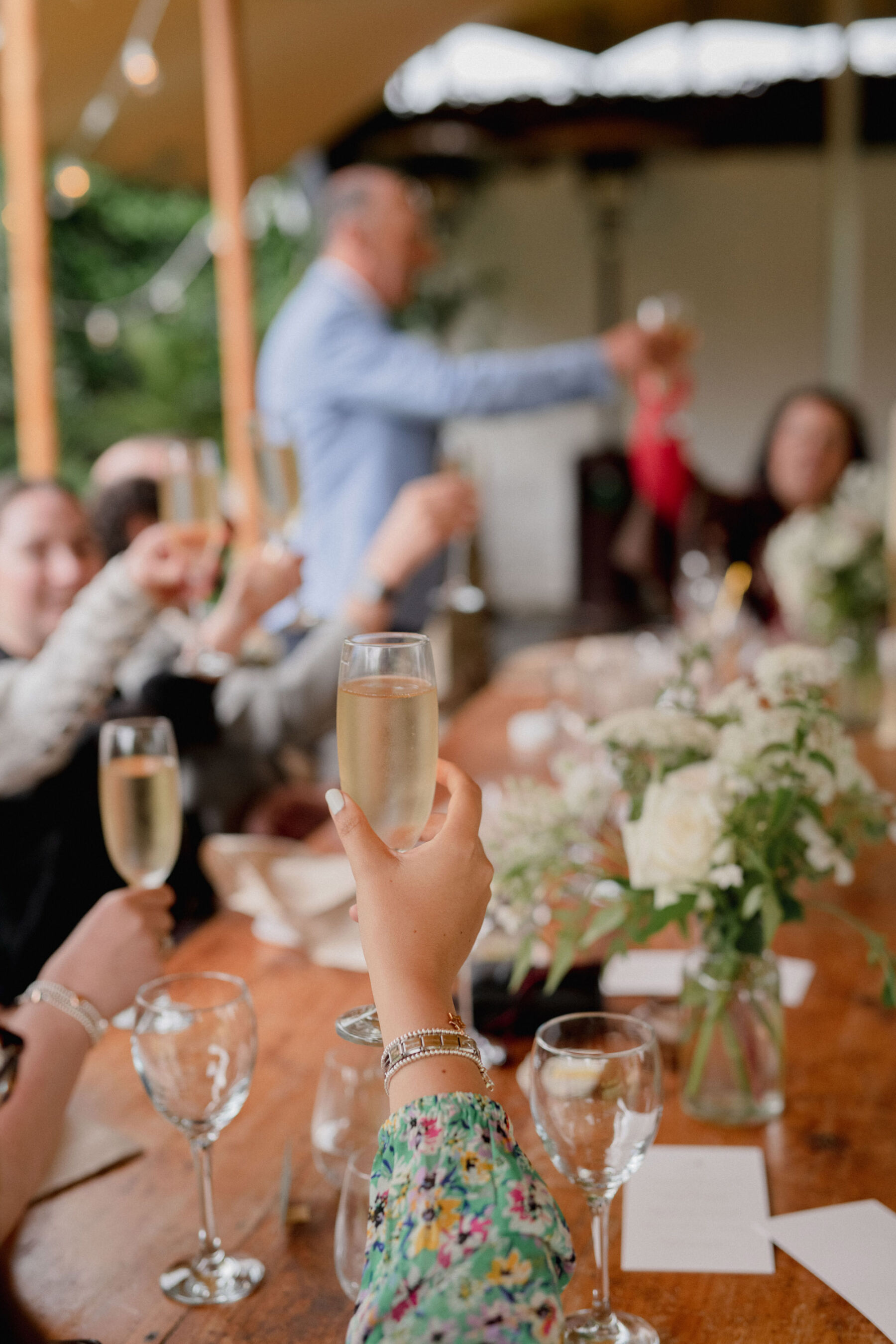 Hands raising glasses of champagne at a wedding. Lyra & Moth Photography.