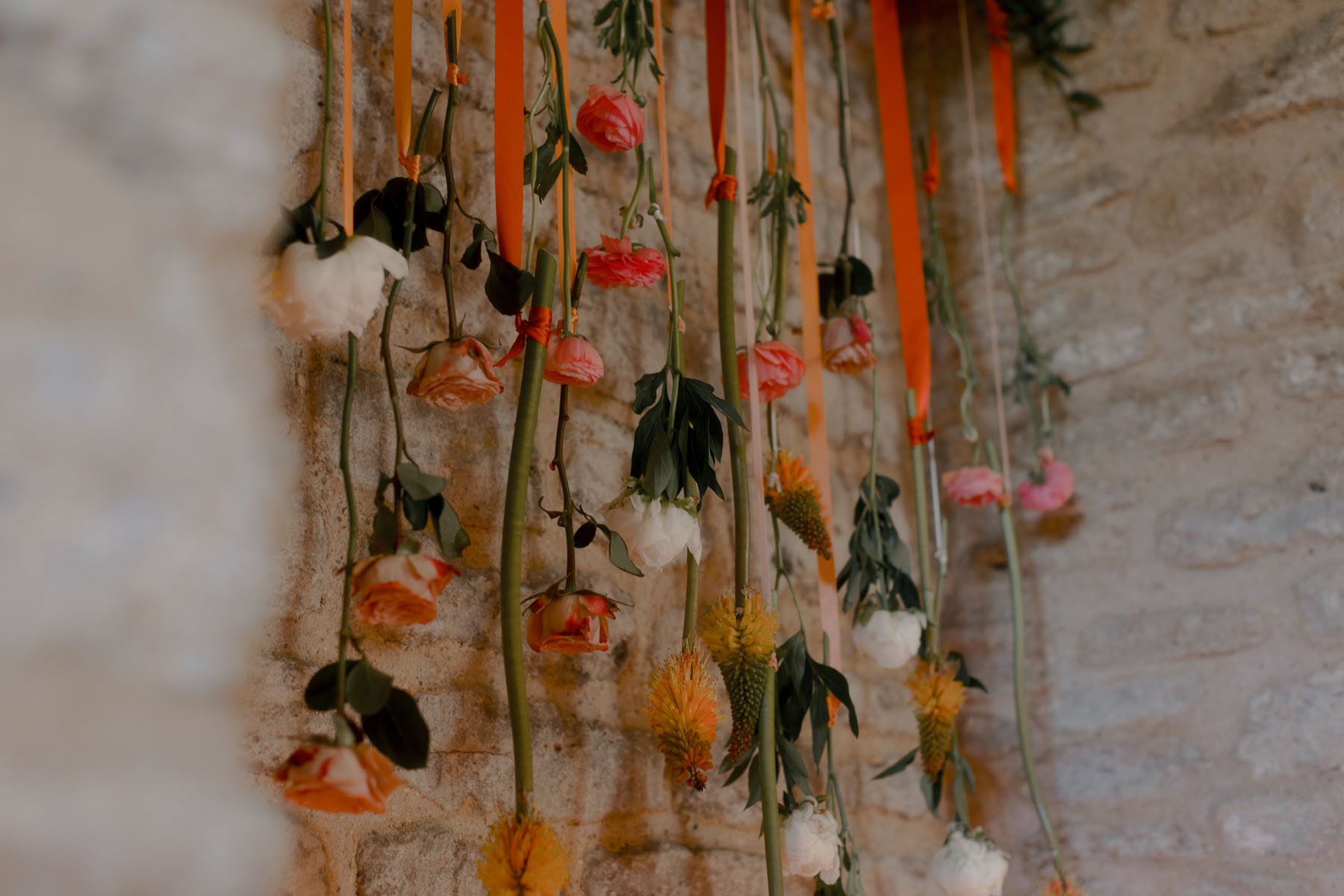 Colourful orange flowers hanging from ribbons at a wedding reception.