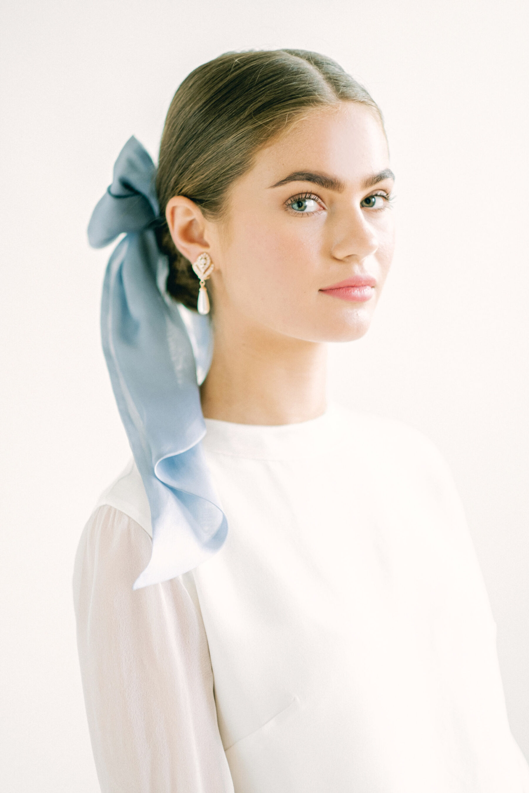 Bride with pale blue silk ribbon in her hair, tied up into a low bun, wearing Kate Beaumont wedding dress.