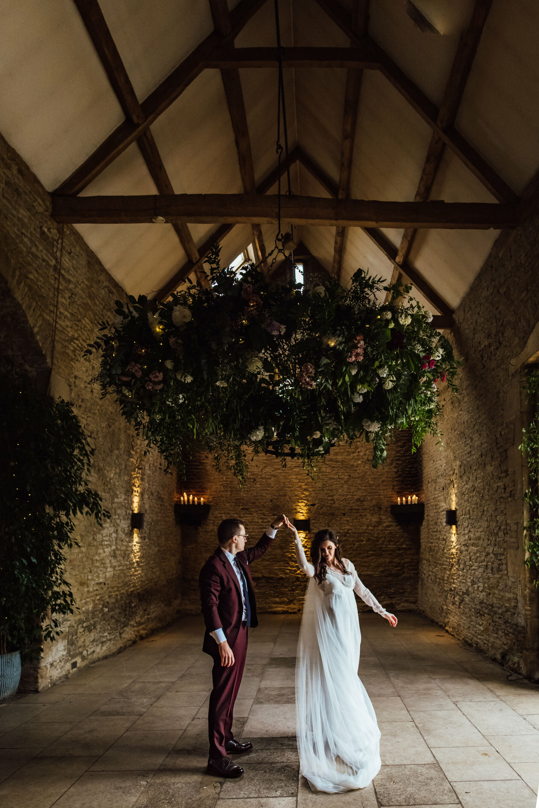 Bride and groom dancing beneath a floral installation at Stone Barn, Cotswolds Wedding Venue