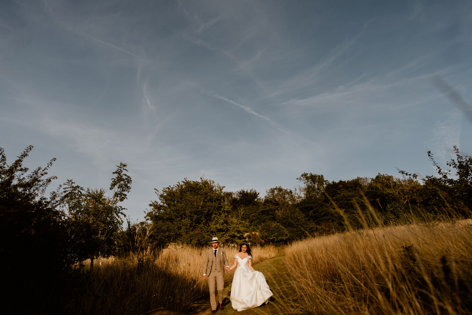 Suzanne Neville bride + groom in pale suit in meadow with tall grasses.