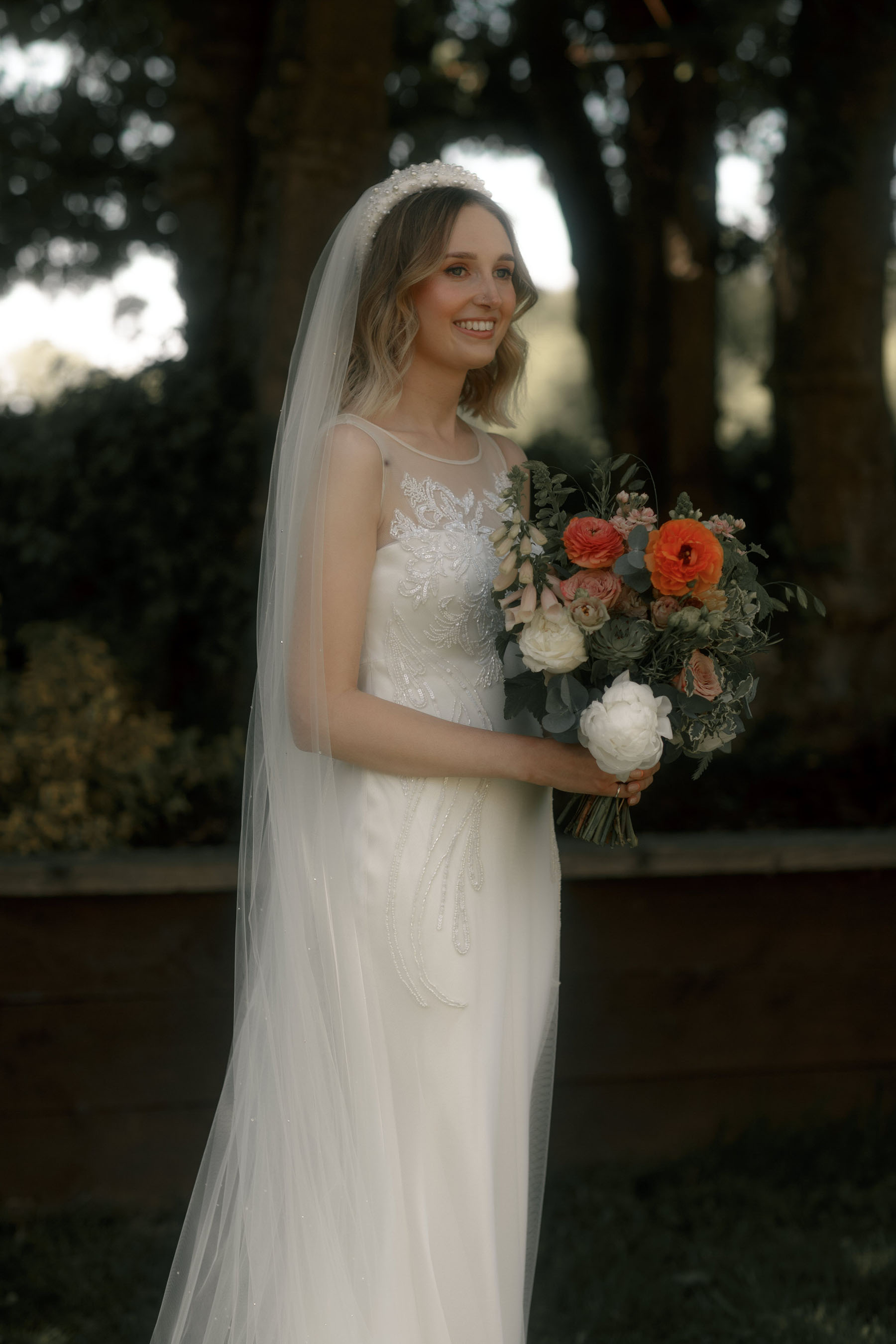 Bride in a Lace & tulle David Fielden wedding dress, a Dolecka eparl headband and long veil. Carrying a white and orange bridal bouquet.