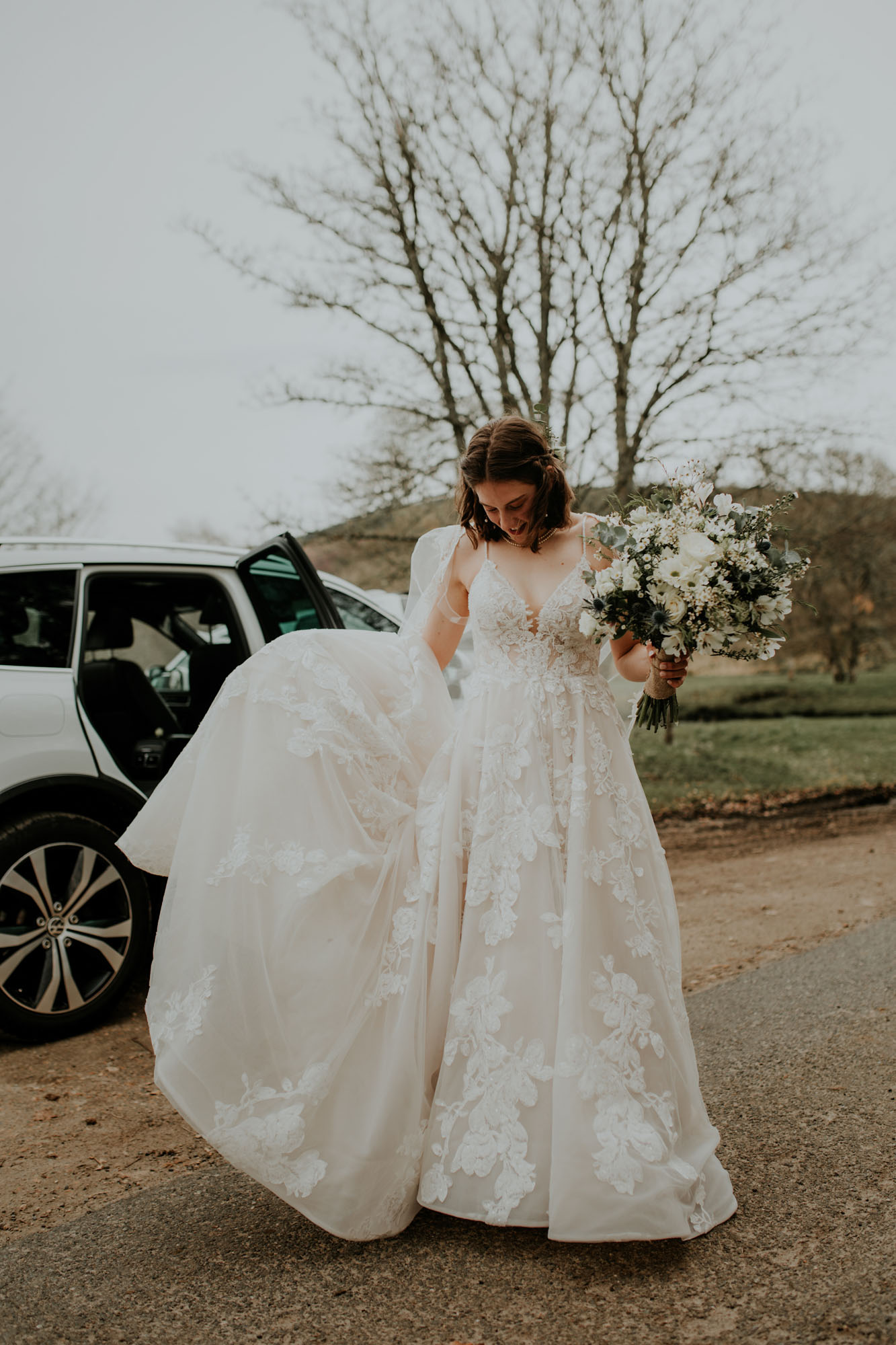 Bride exiting a wedding car with a beautiful lace wedding dress & bridal cape