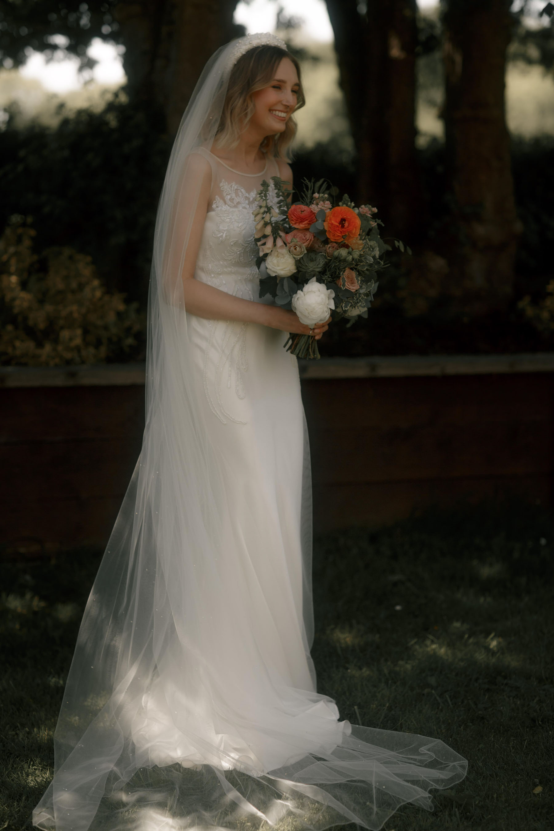 Bride in David Fielden wedding dress, long veil, pearl headband and colourful orange wedding bouquet.