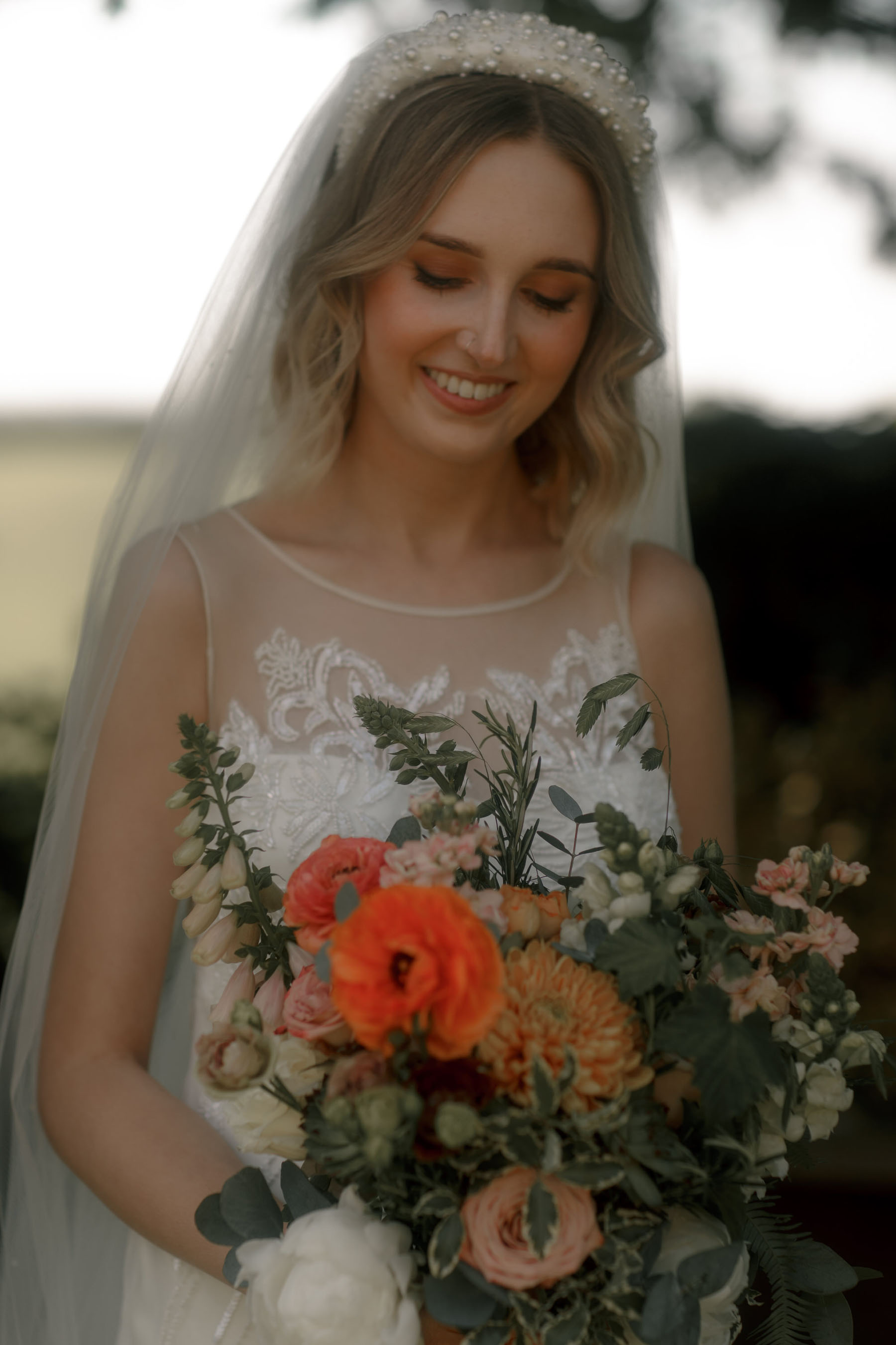 Bride in David Fielden wedding dress, long veil, pearl headband and colourful orange wedding bouquet.