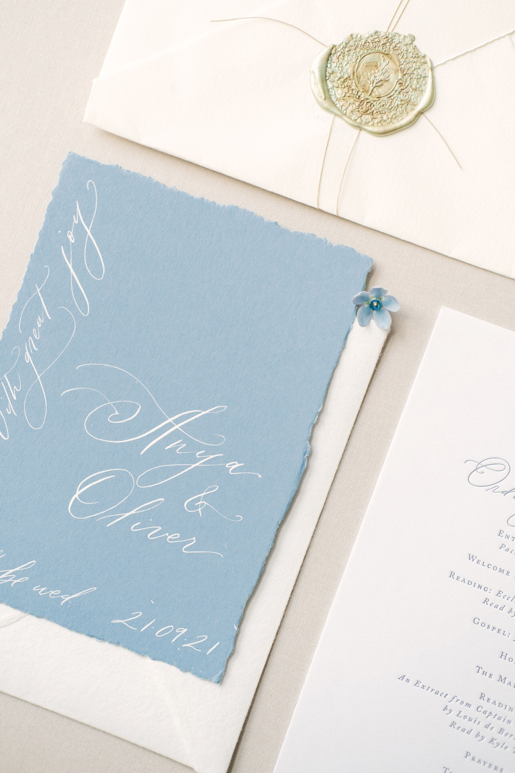 Pale blue wedding stationery with white ink calligraphy & gold wax stamp.