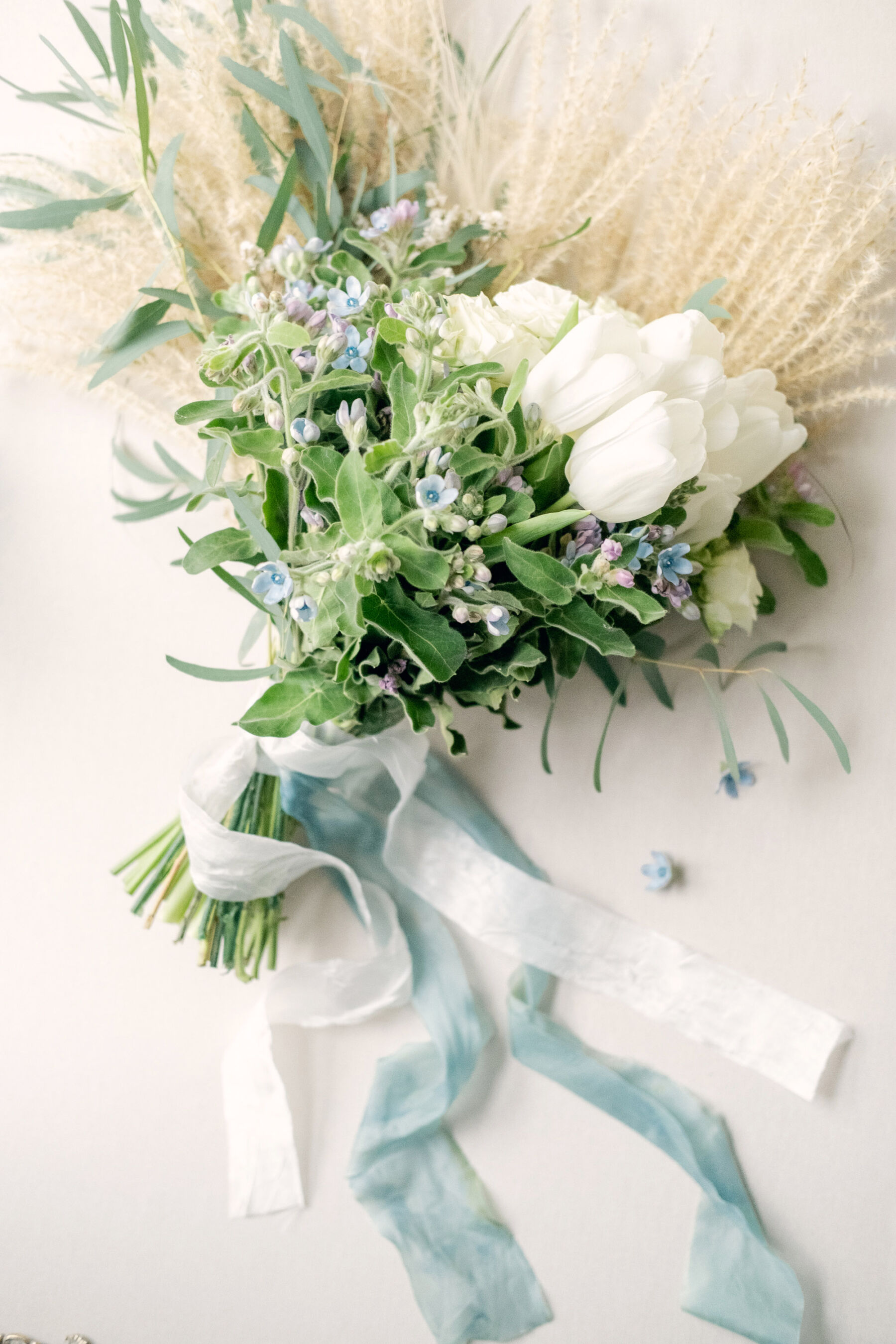 English flowers wedding bouquet with roses and Tweedia. Cream and pale blue silk ribbons tied around the flowers.