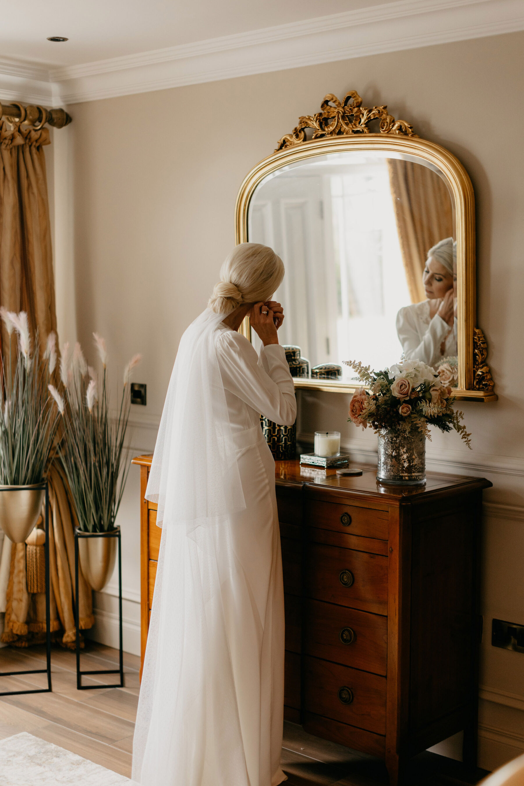 Bride with low bun looking in to a mirror, wearing a Rixo wedding dress & veil.