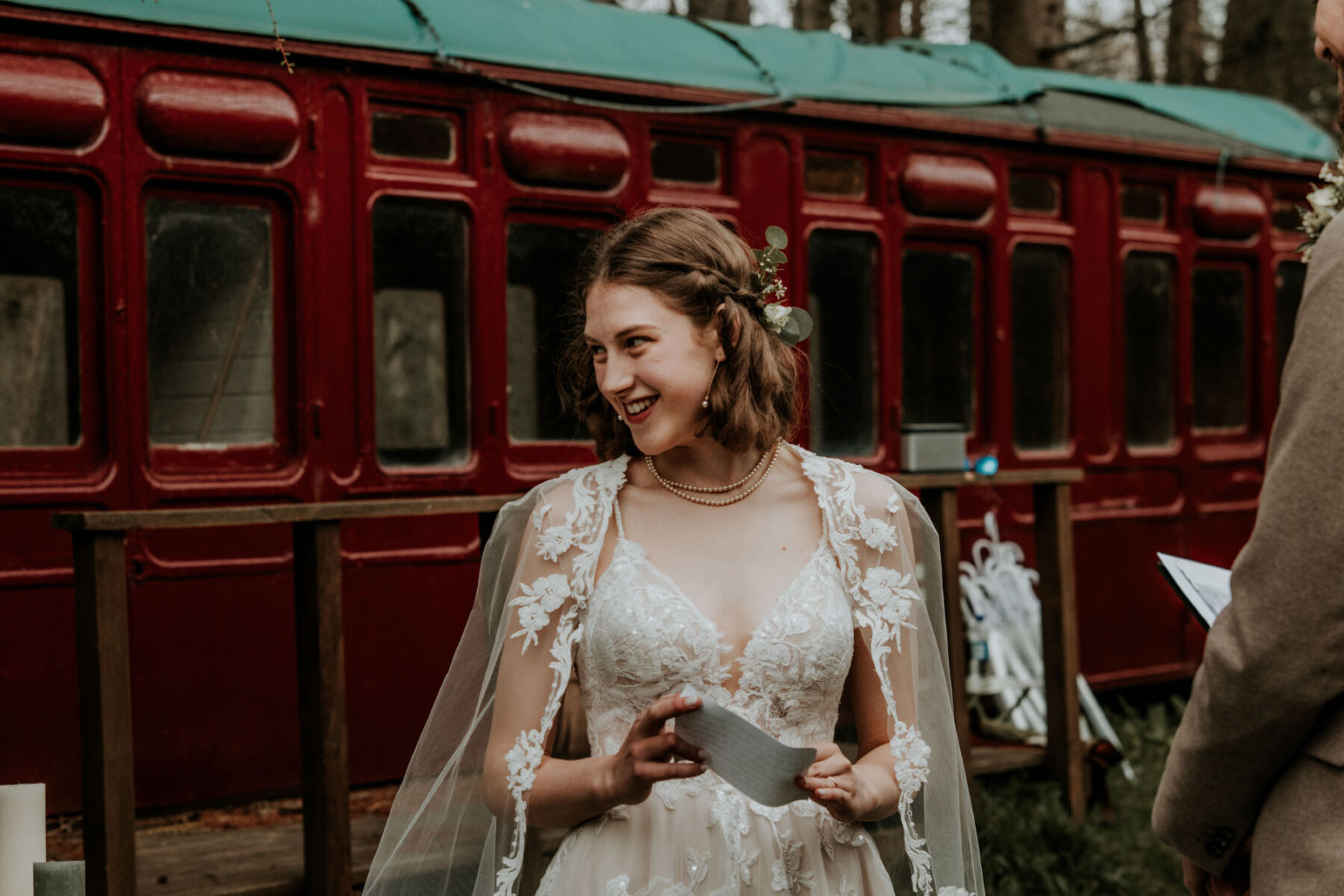 Bride in lace dress and bridal cape standing by an old train carriage
