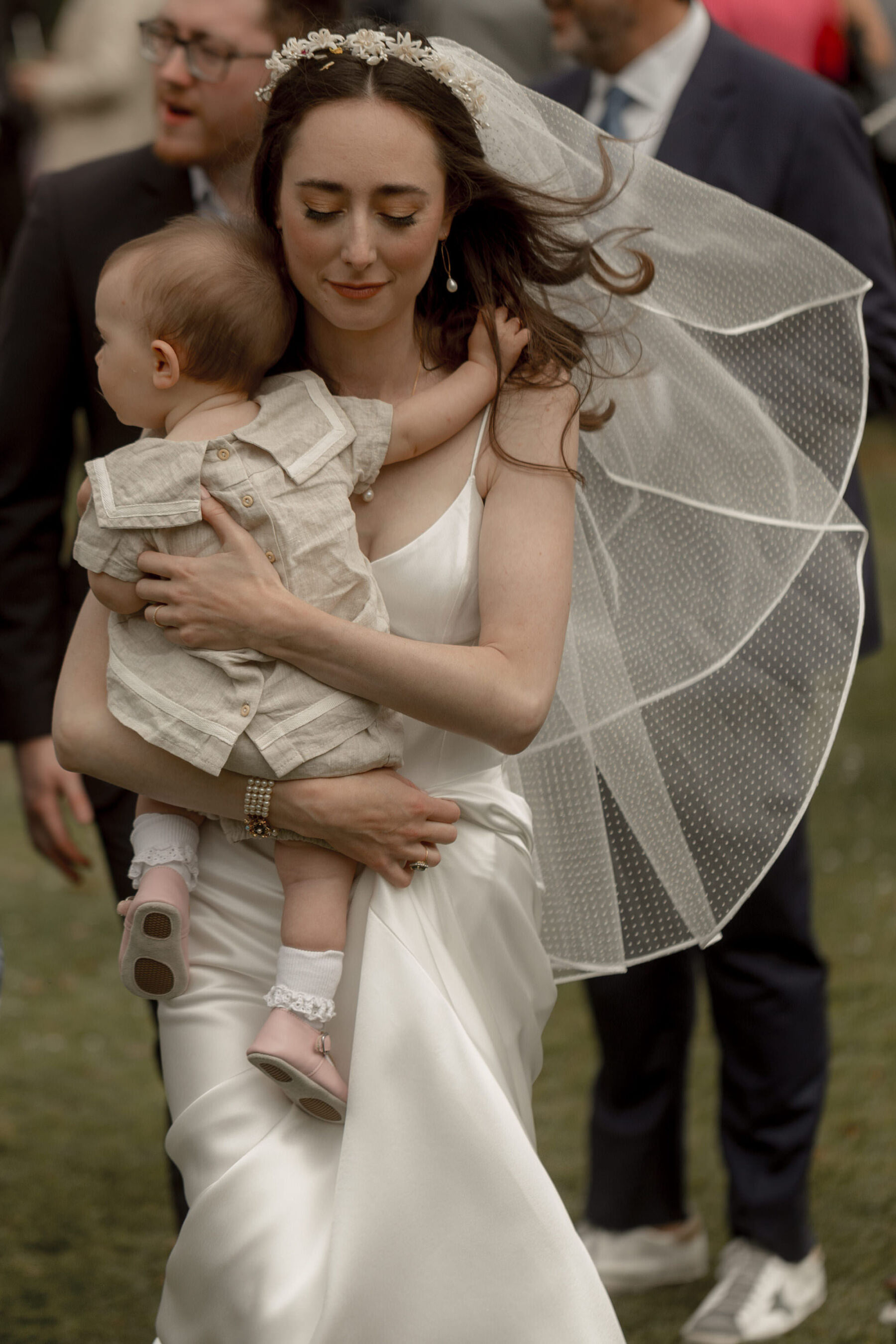 Bride in Galvan wedding dress, polka dot veil, carrying baby flowergirl.