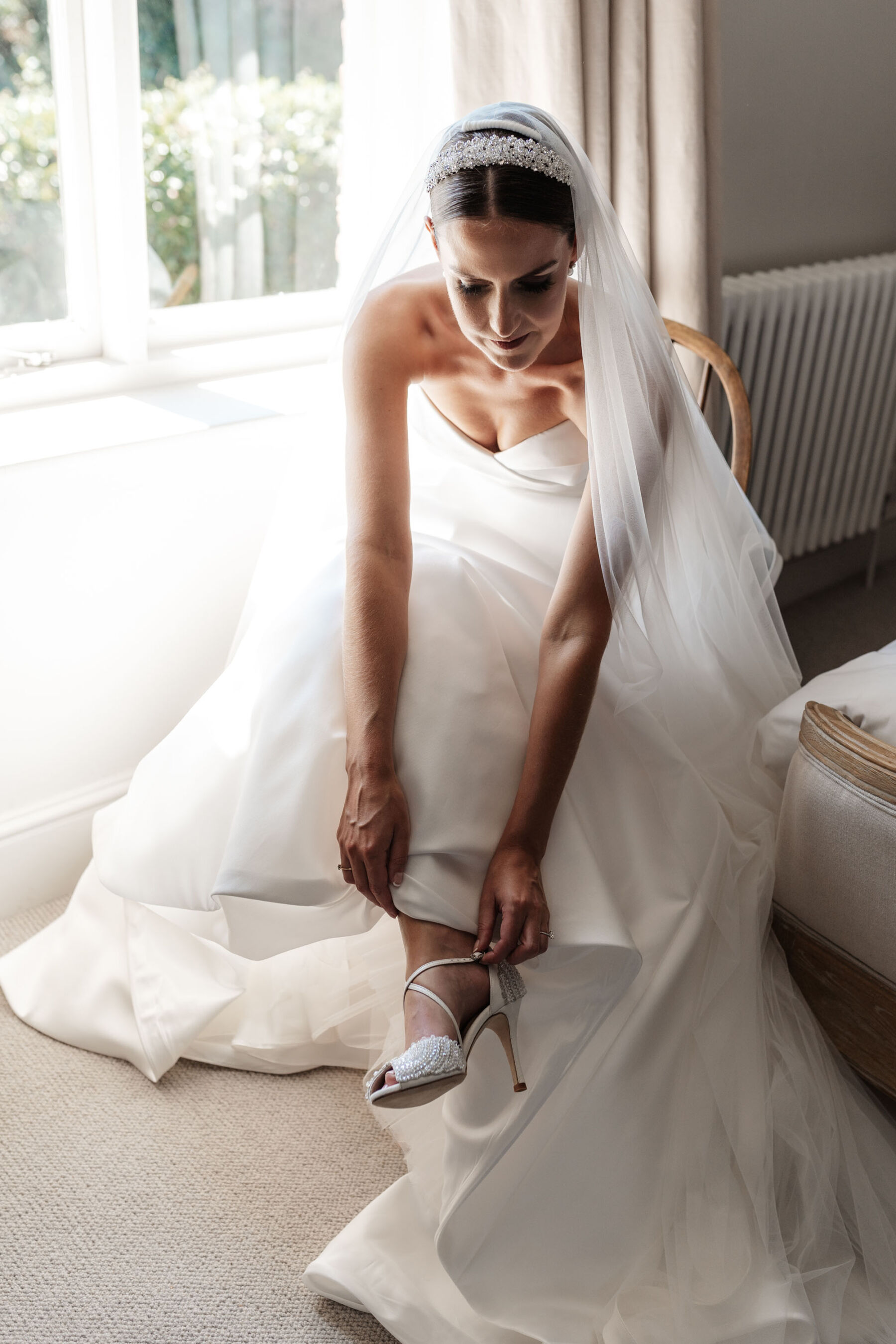 Bride putting on Emmy London wedding shoes on the morning of her wedding. Suzanne Neville wedding dress.