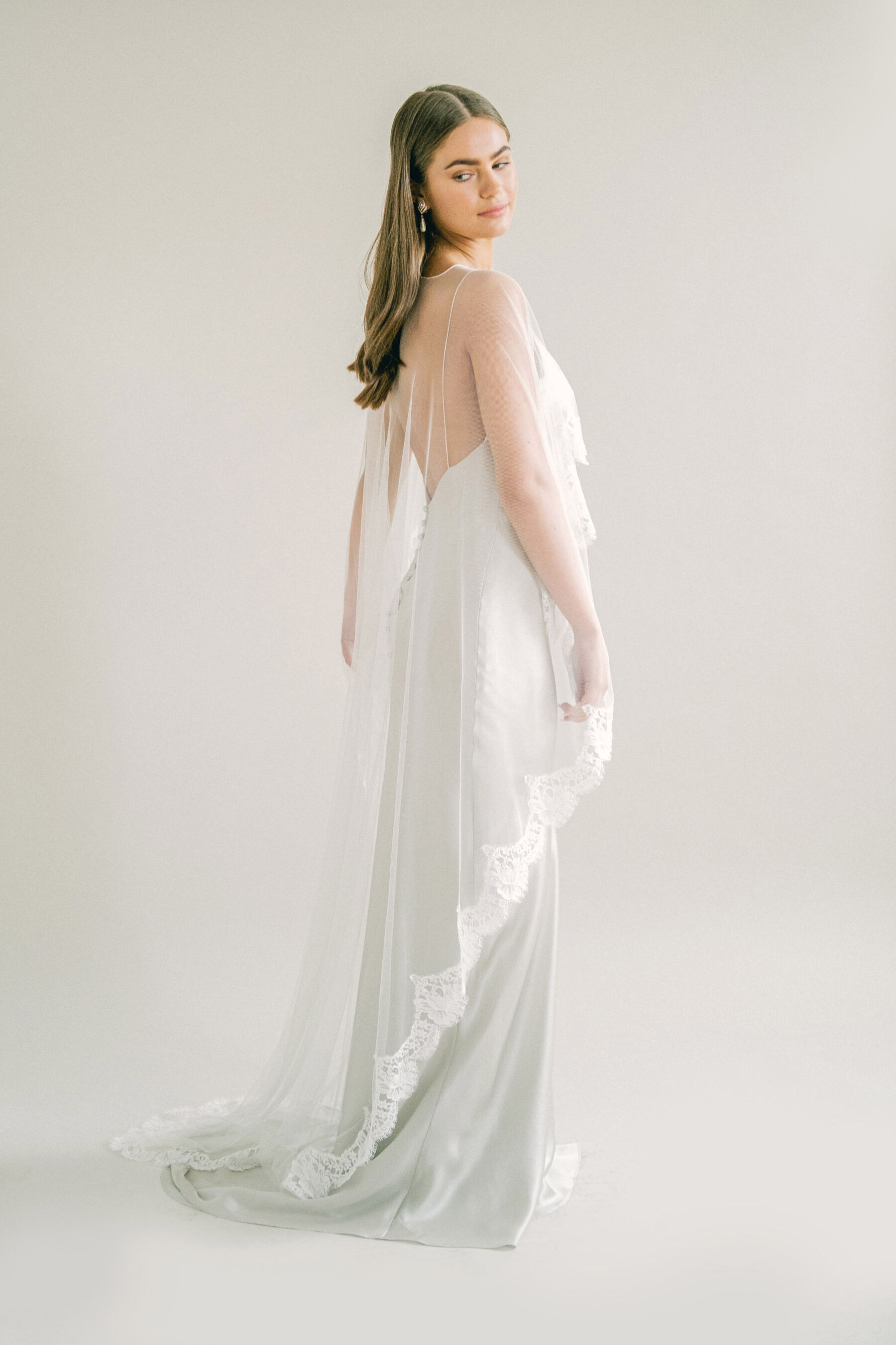 Bride wearing a Kate Beaumont slip dress with veil cape that is longer at the back.