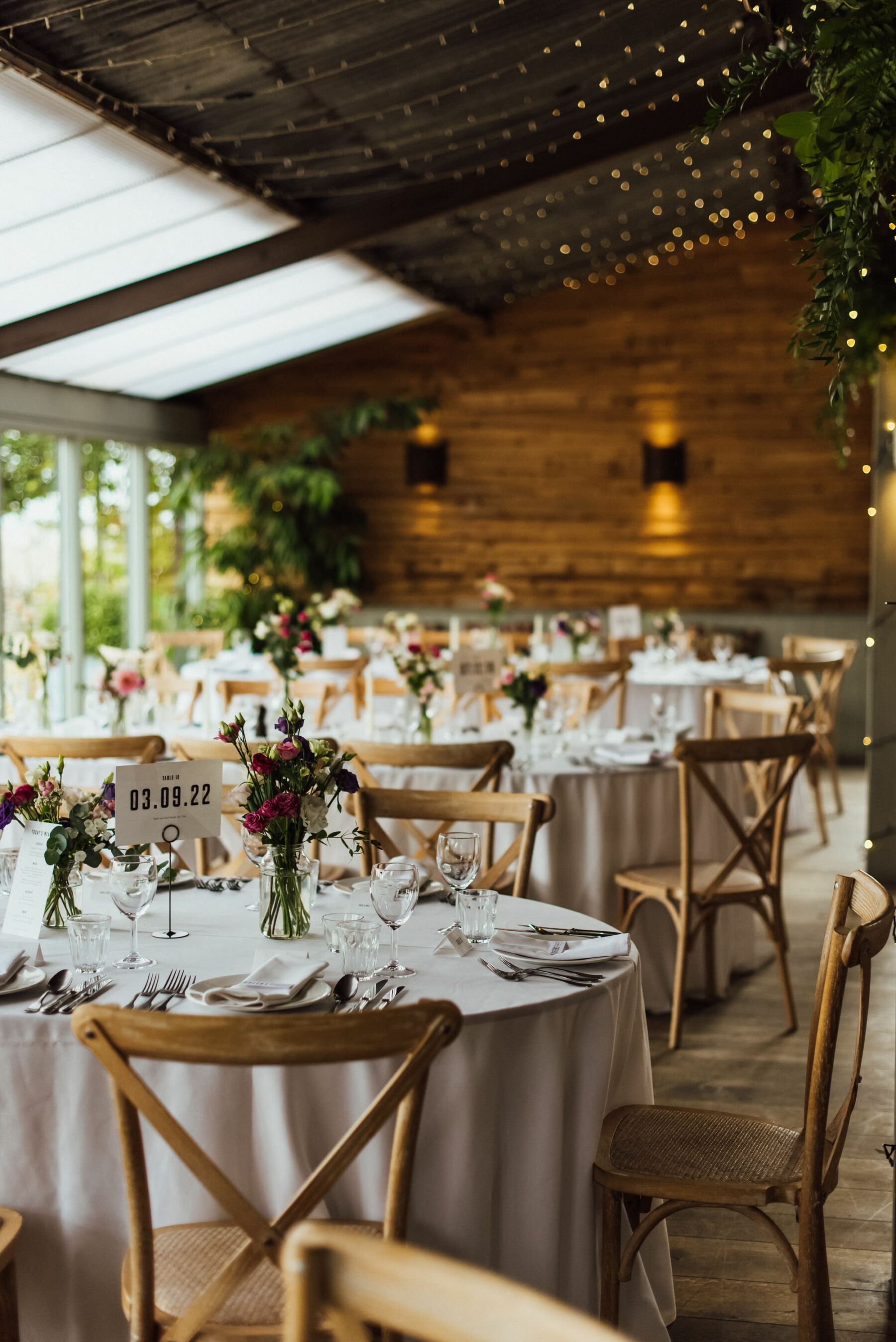 Fairylights canopy hanging over tables & crossback chairs at Stone Barn, Cotswolds Wedding Venue