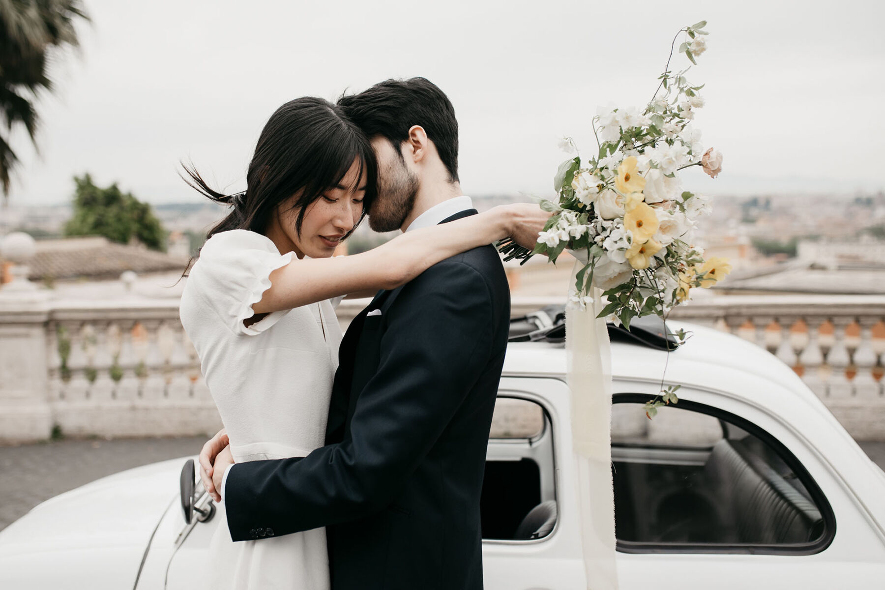 Chinese bride in a Laure de Sagazan dress holding a Spring wedding bouquet. Fiat 500. Elopement in Rome.