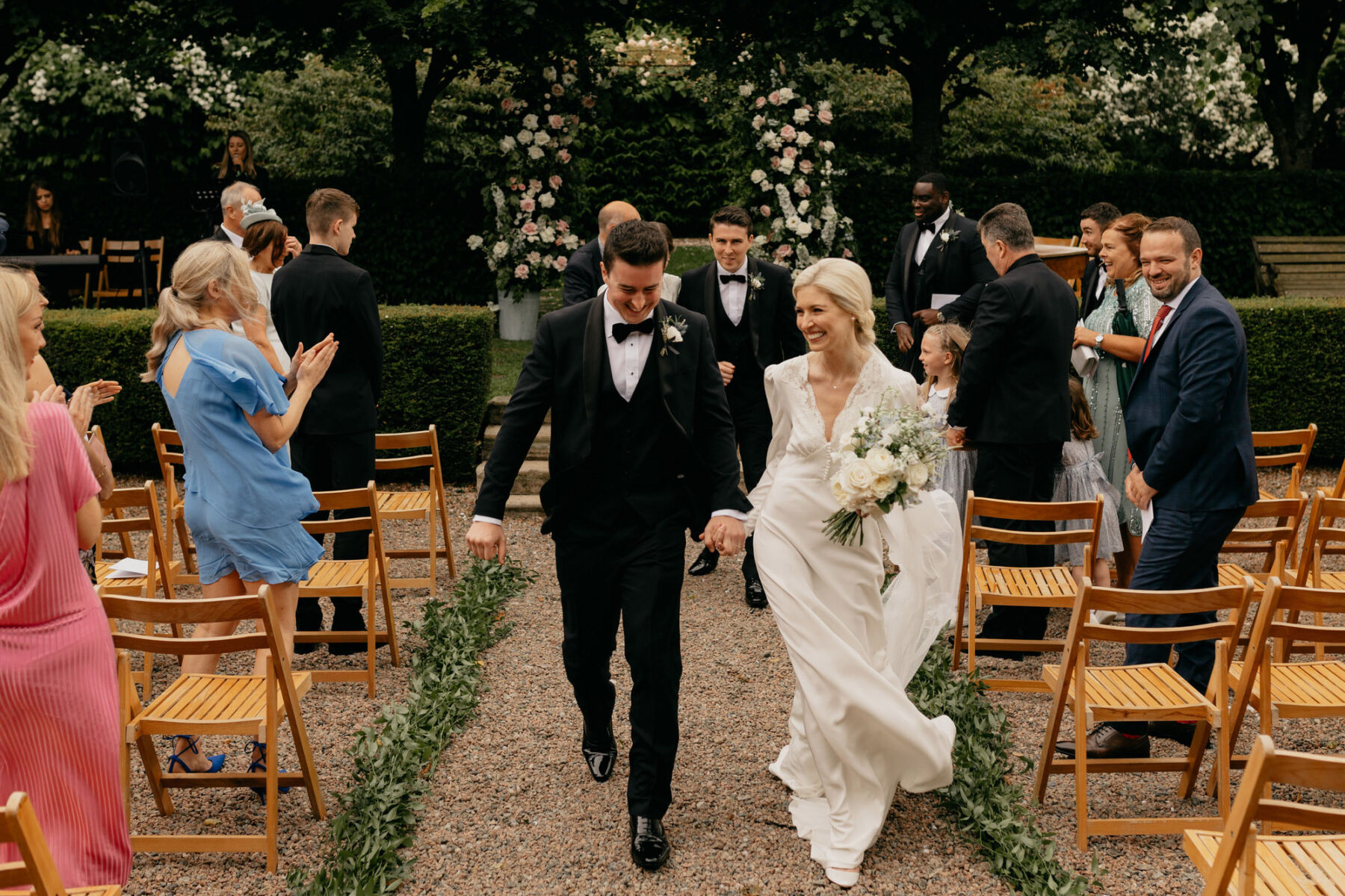 Bride and groom just married in the gardens at Larchfield Estate, Co Down Northern Ireland. Bride wears a Rixo wedding dress and veil. Groom in black tie.