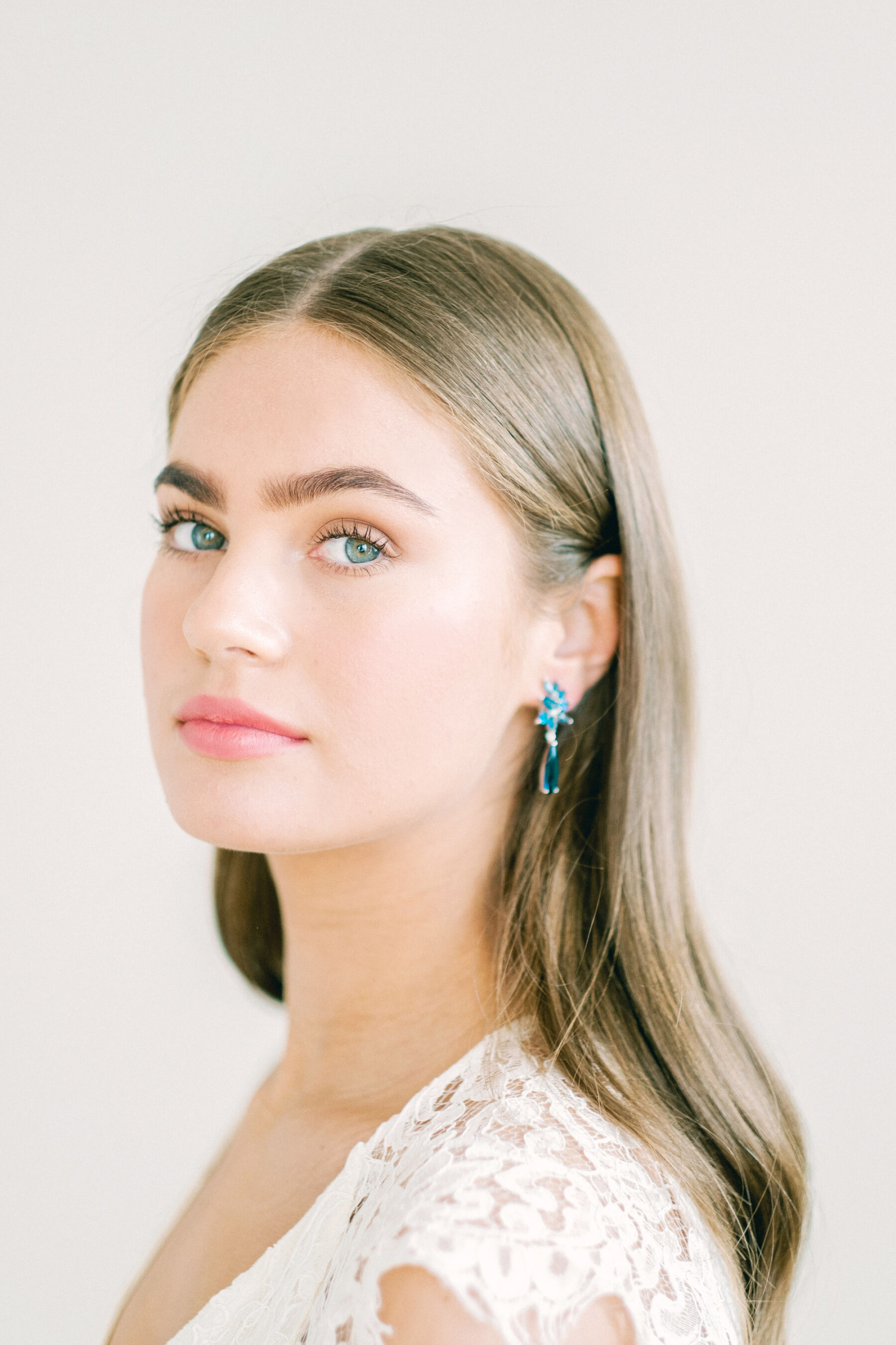 Face portrait of elegant bride with centre parting and long brown hair wearing blue drop earrings.