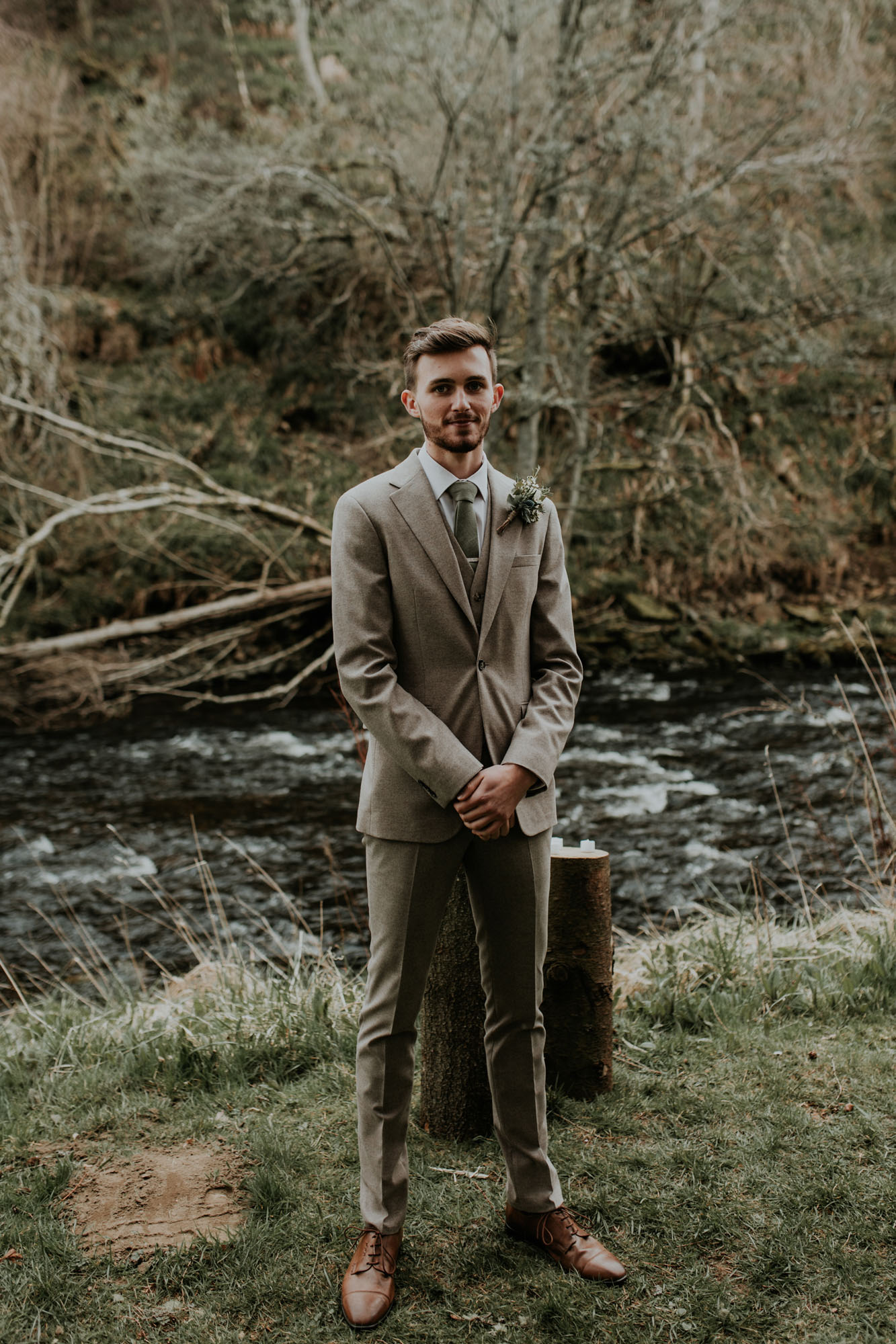Groom standing in a pale brown Moss Bros wedding suit