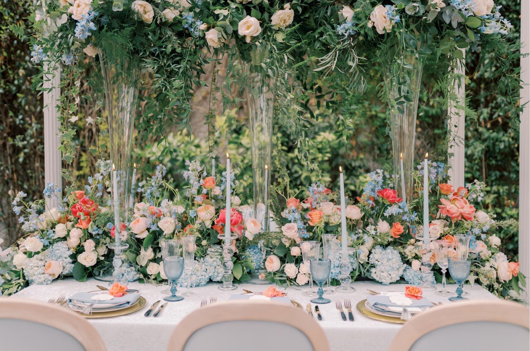 Pale blue glasses, candles, colourful floral wedding table decor. Westacott Weddings & Events