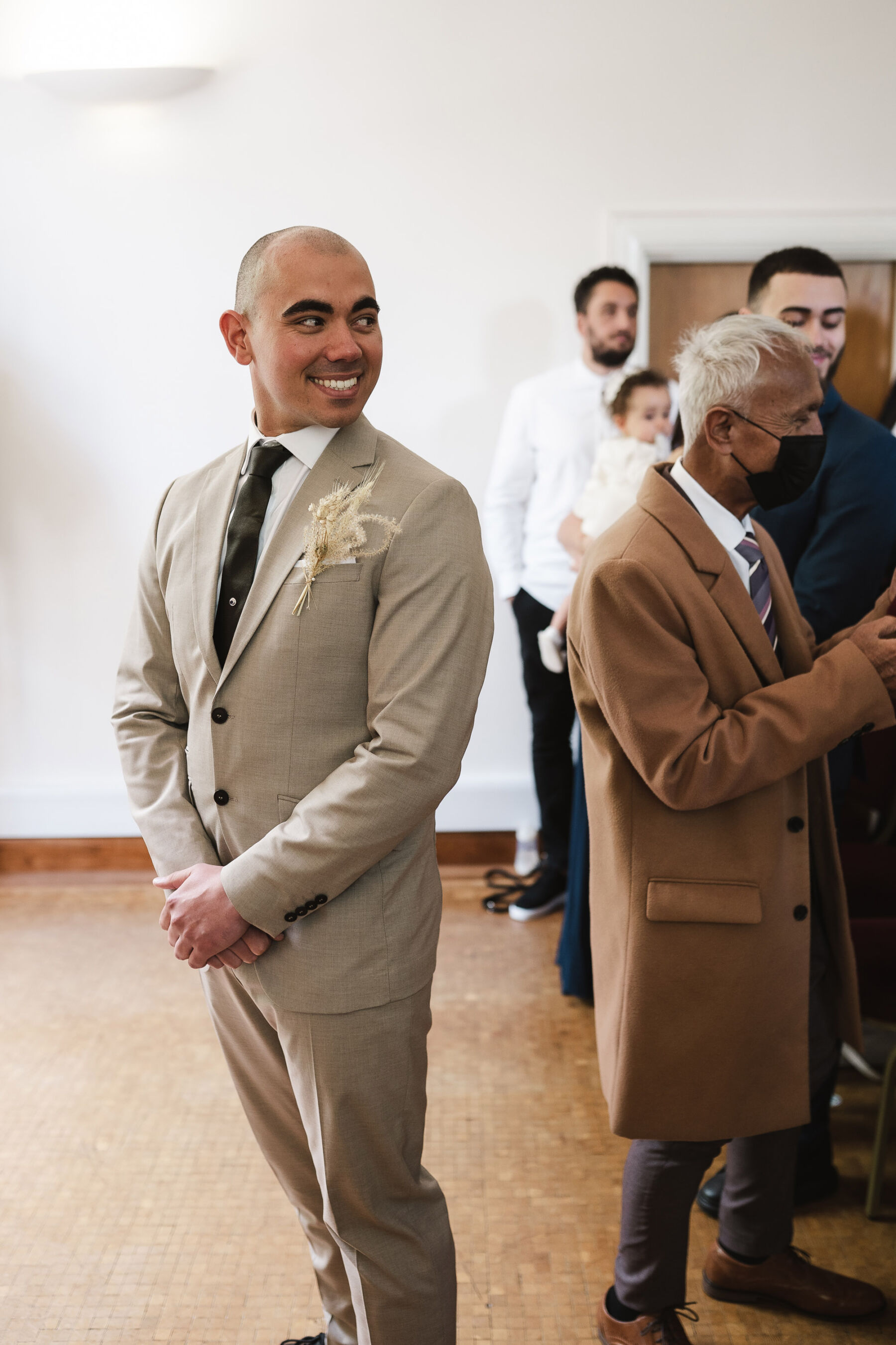 Happy groom in light beige suit smiling as his bride arrives. By Karolina Photography.