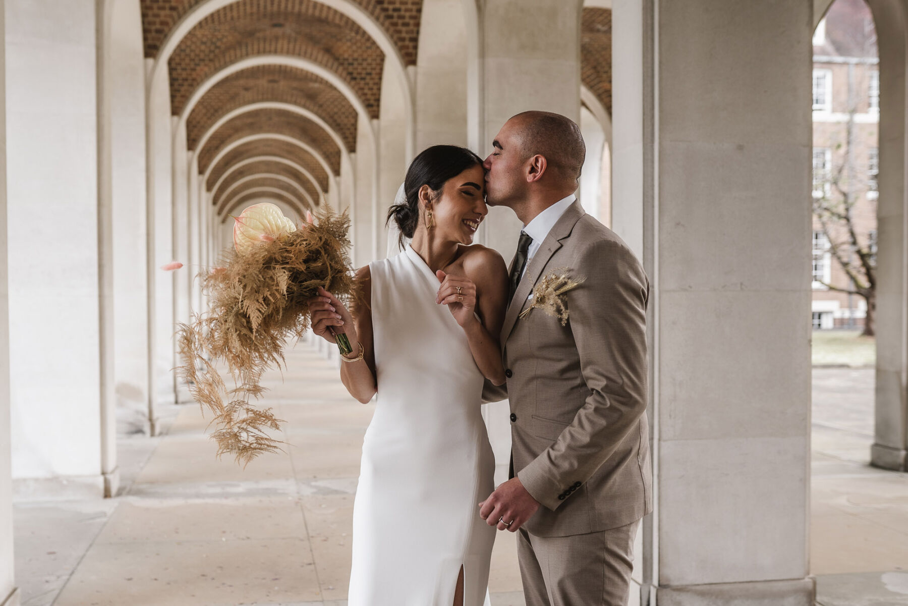 Bride carrying bleached fern bridal bouquet. Solace London wedding dress. By Karolina Photography.