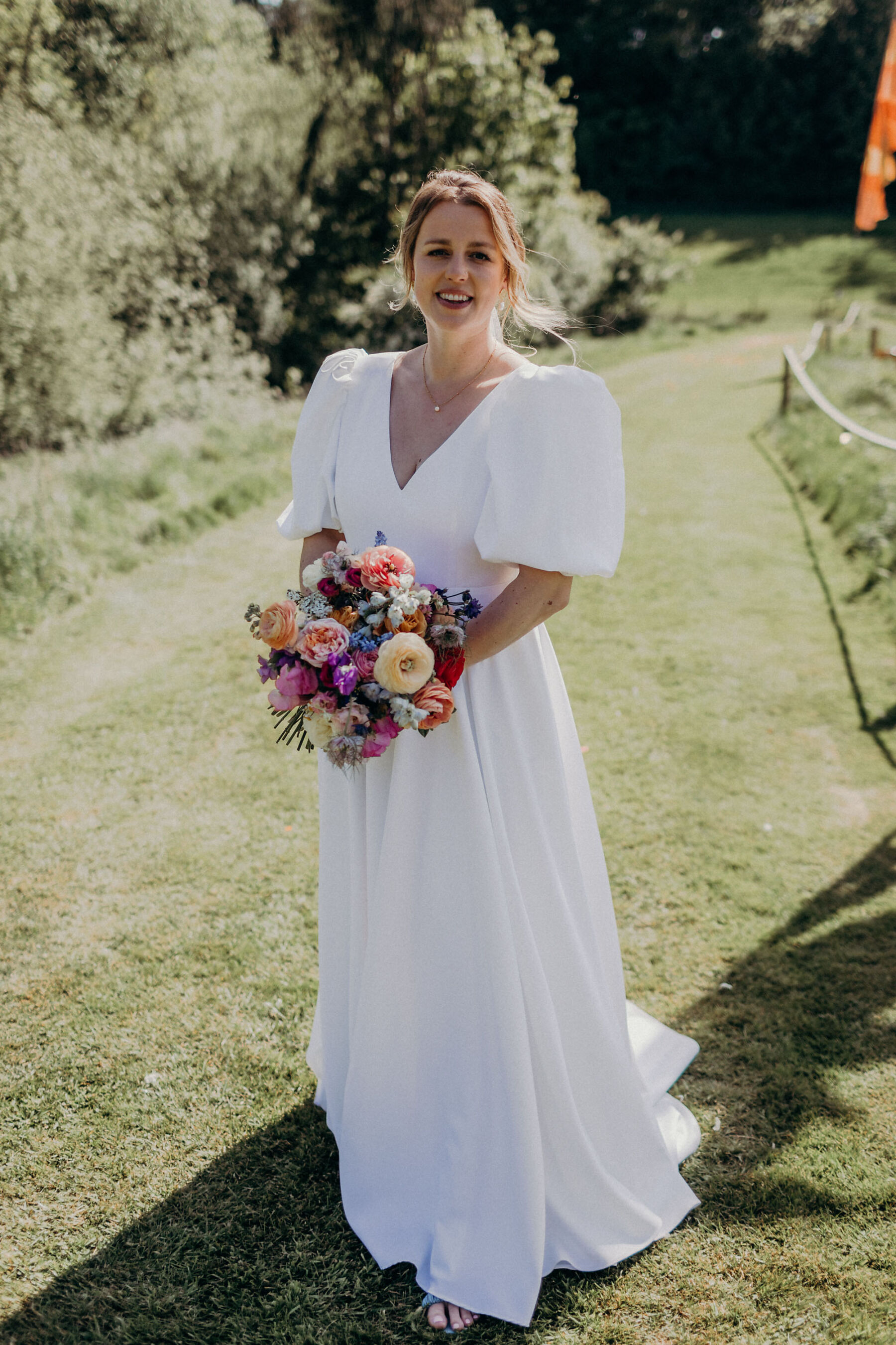 Happy bride holding a colourful wedding bouquet, wearing the Audlyn wedding dress, by & For Love.