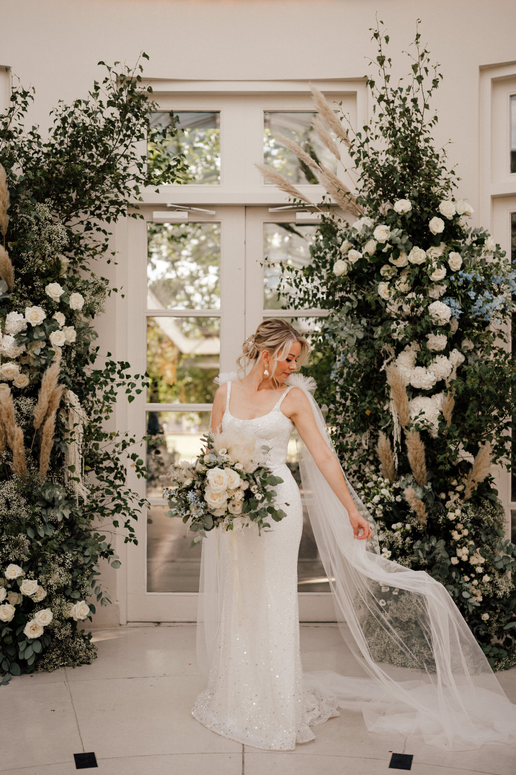Bride in a Kyha Studios wedding dress standing in front of a broken floral arch