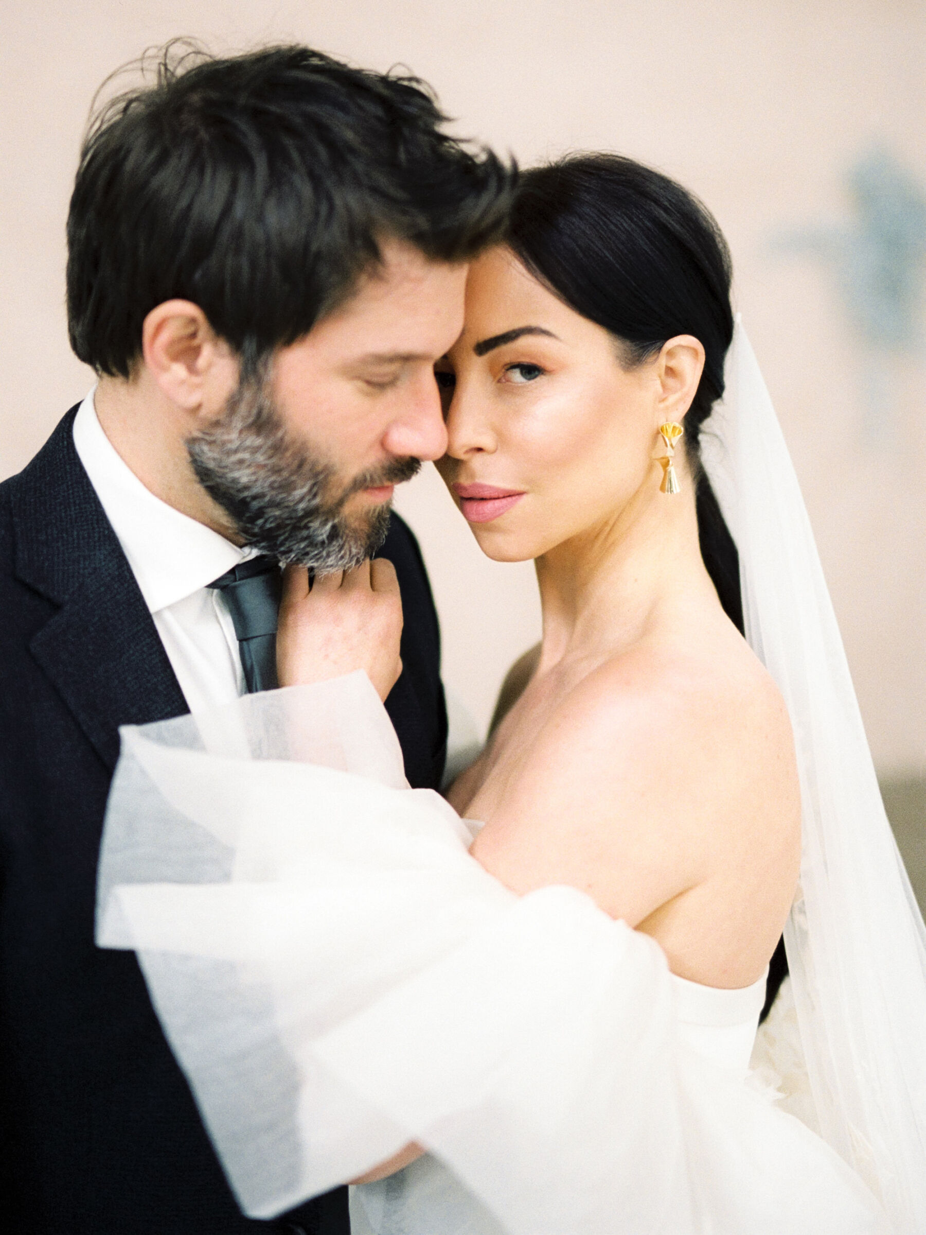 Bride and groom embracing. Bride with modern ponytail and pearl drop earrings.