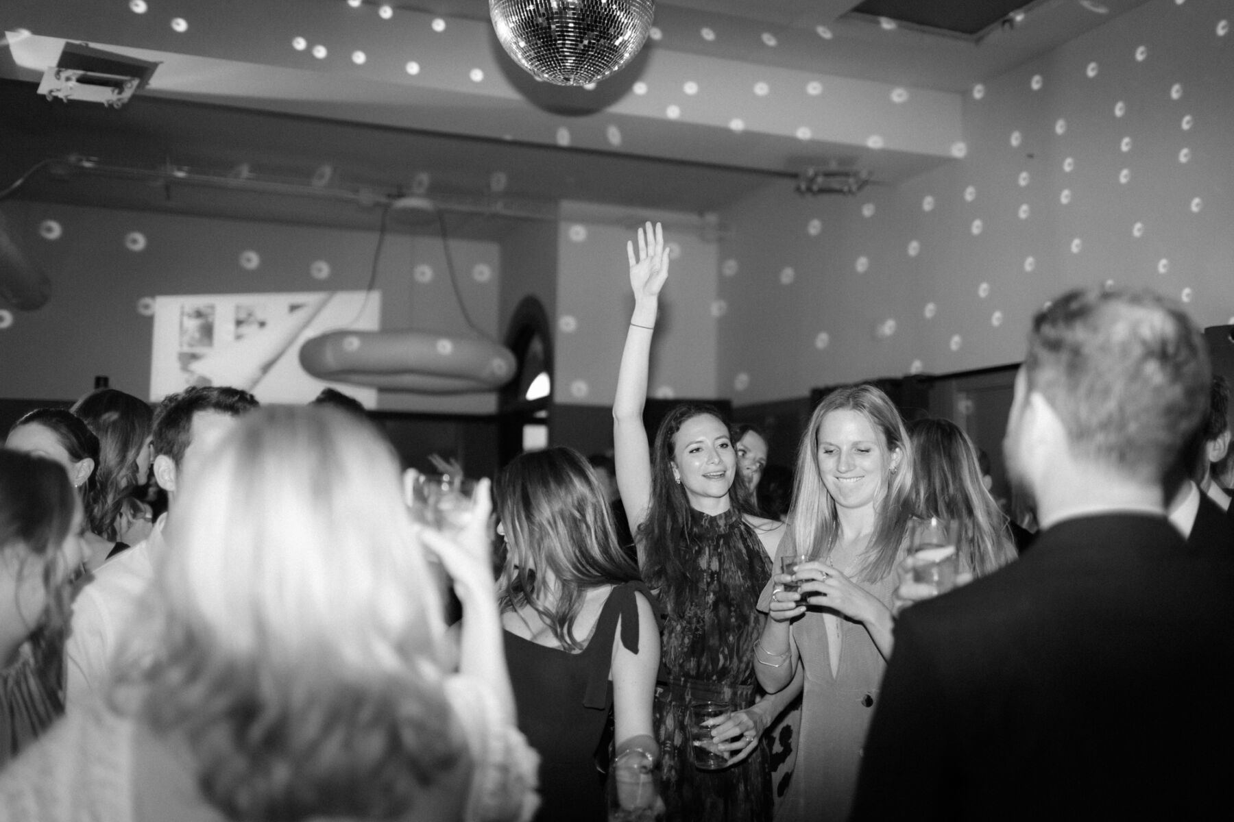 Guests raising their hands on the dance floor underneath a glitter ball. Rebecca Rees Photography.