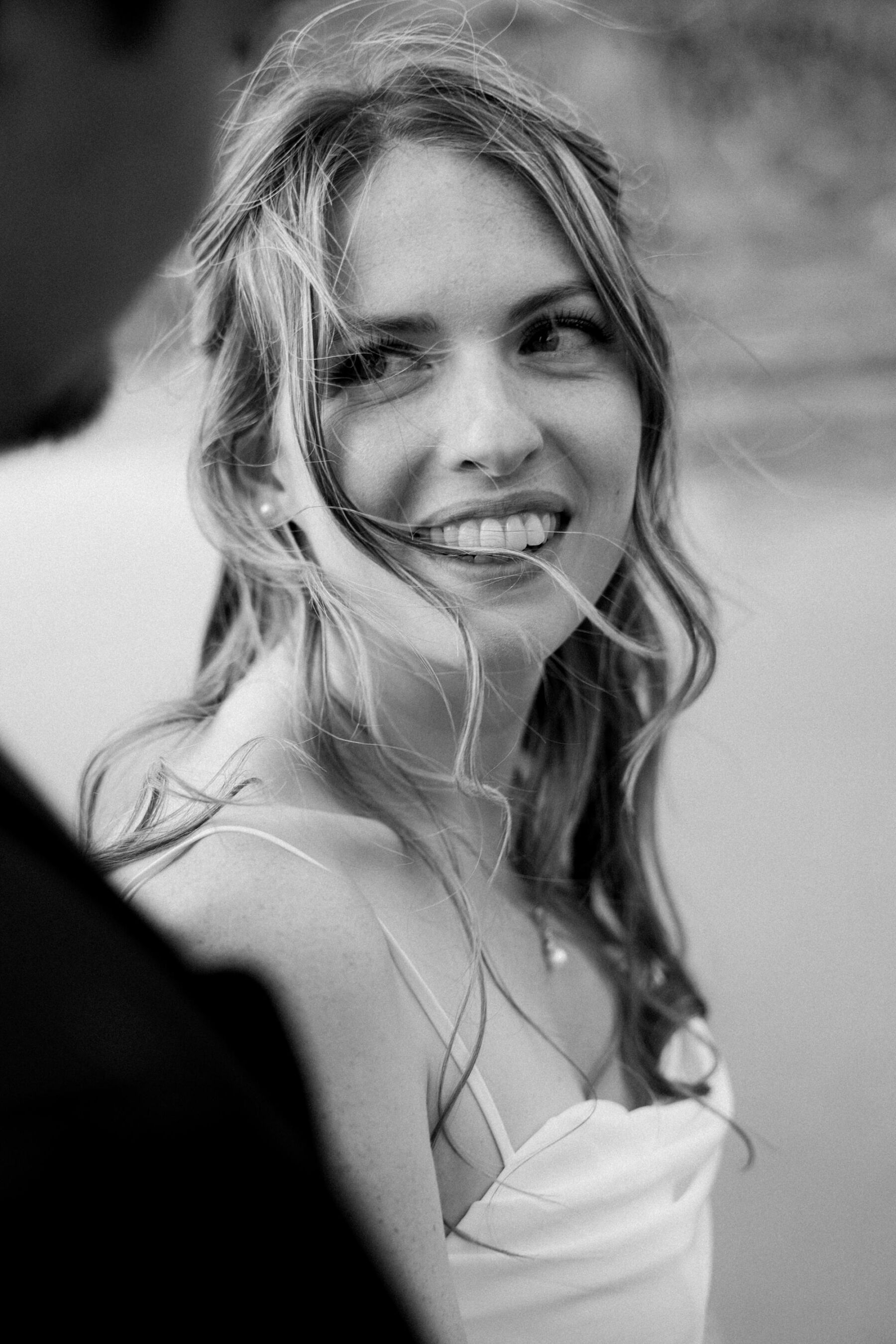 Black and white shot of bride with windswept hair gazing lovingly at her groom.