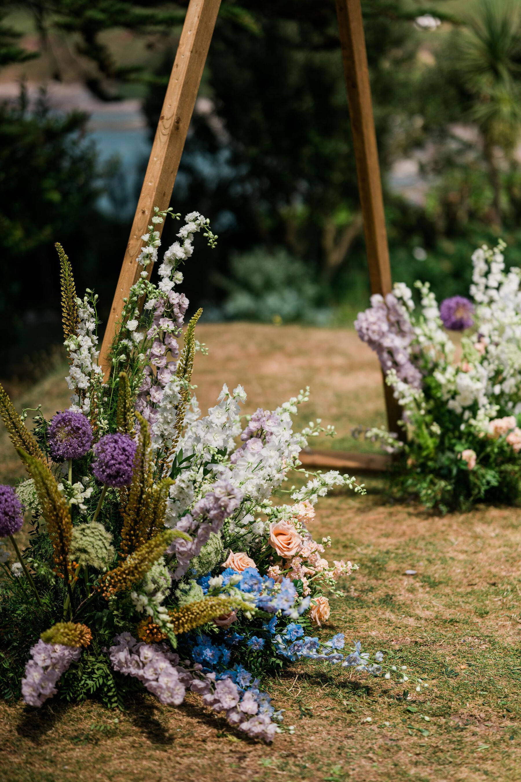 Beautiful seasonal summer flowers sitting at the base of an outdoor wedding ceremony backdrop