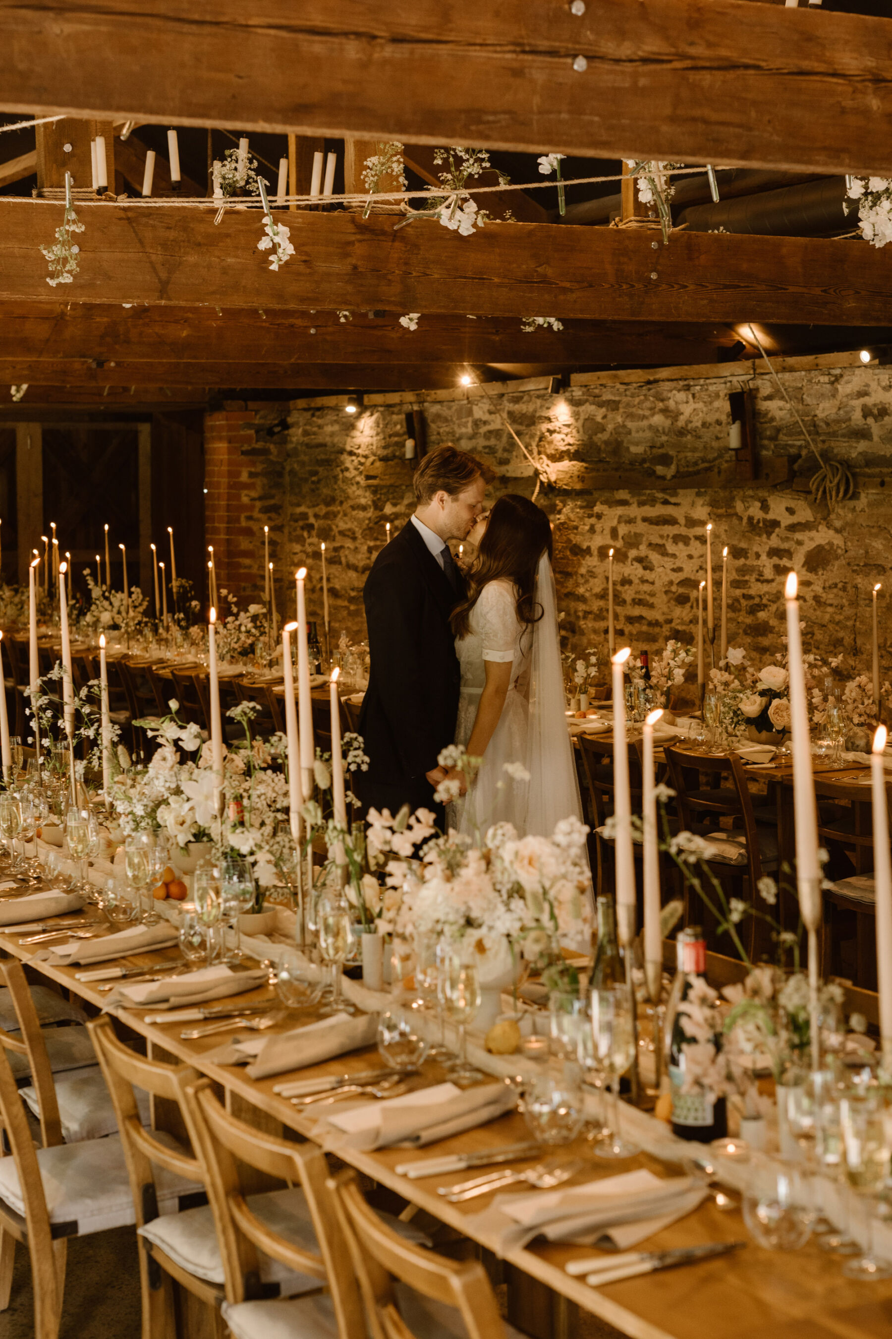 Wedding reception at Dewsall Court. Long wooden trestle tables with tall pink taper candles and pastel flowers. Agnes Black Photography.