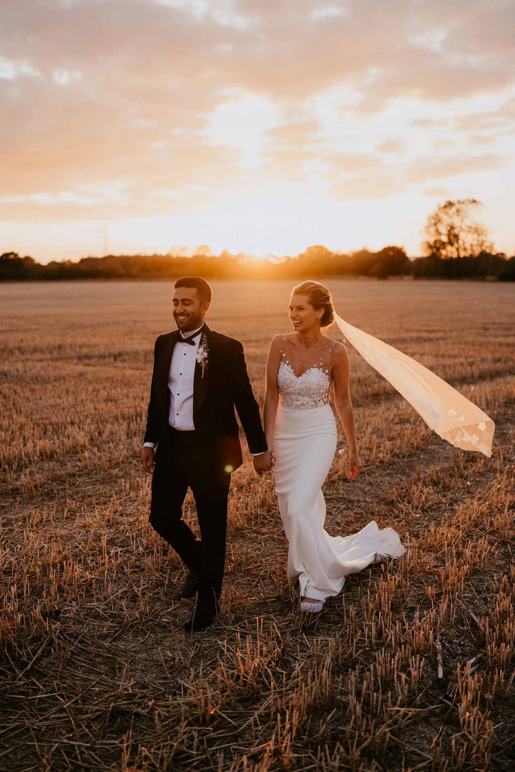 Glamorous bride and groom in a field at golden hour.